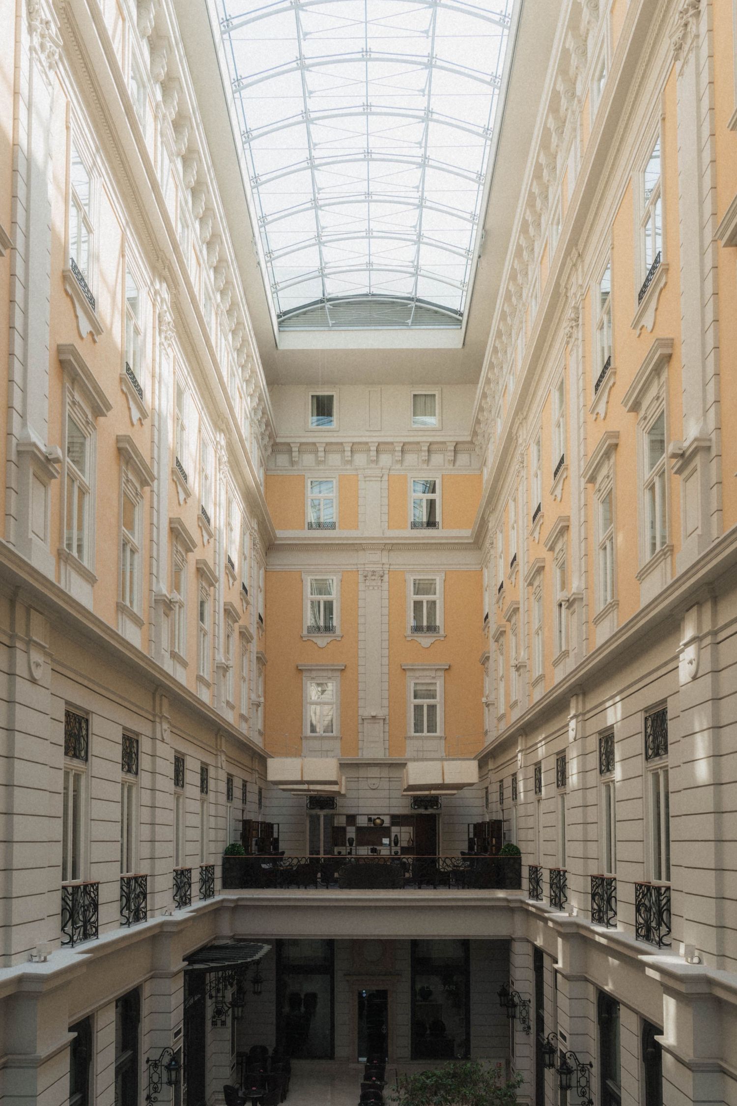 Elegant indoor courtyard with glass skylight ceiling, yellow facade, ornate balconies, and classical European architecture.