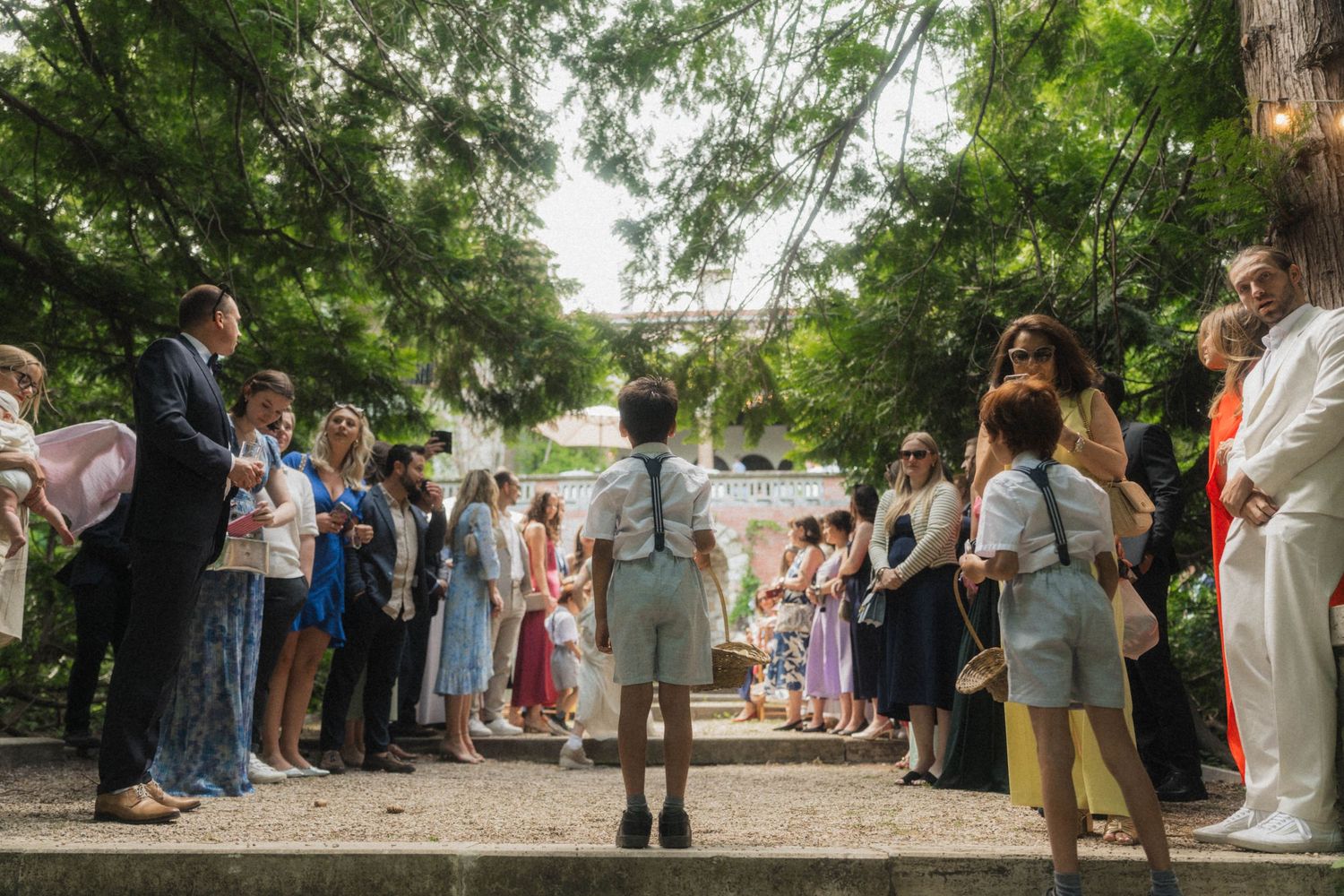 Wedding guests gathered outdoors under lush green trees for an elegant garden ceremony.