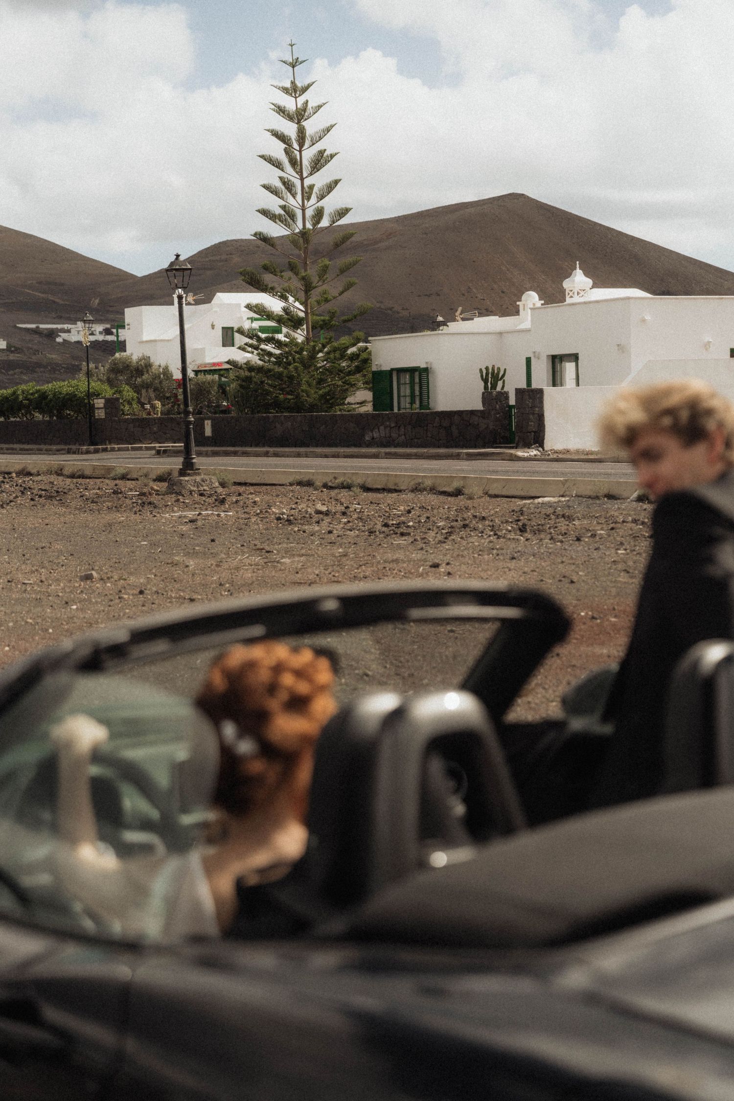 Bride with updo sits in black convertible car at volcanic landscape wedding venue.