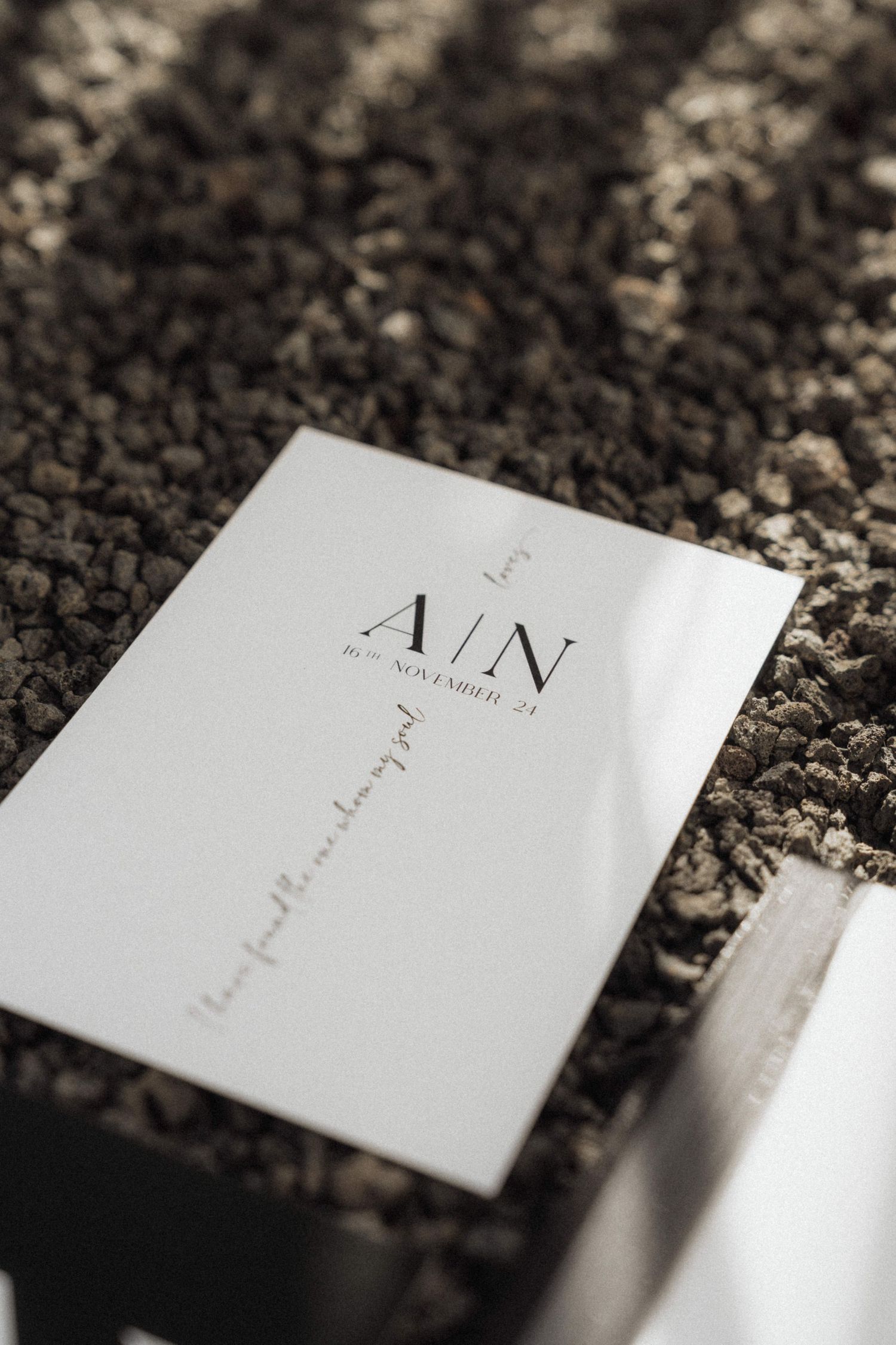 Minimalist white wedding invitation card with A/N monogram and November date on volcanic rock.
