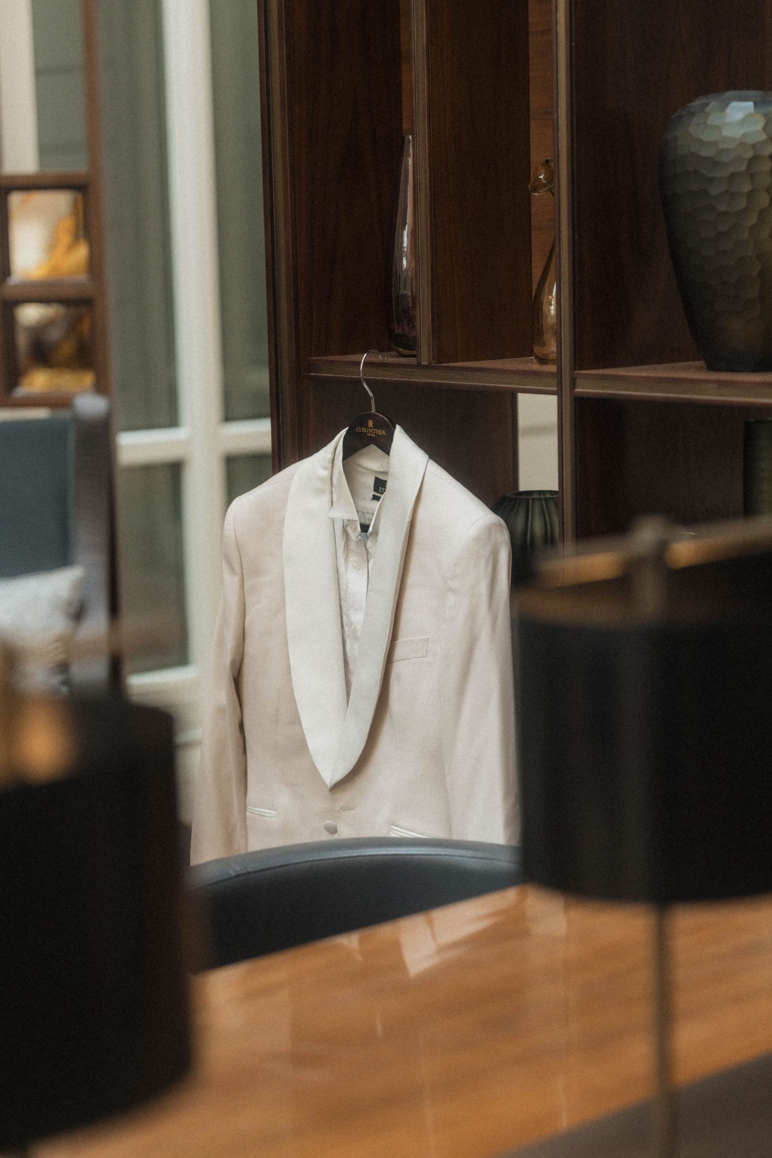 White tuxedo jacket on hanger displayed in elegant wooden wardrobe setting.