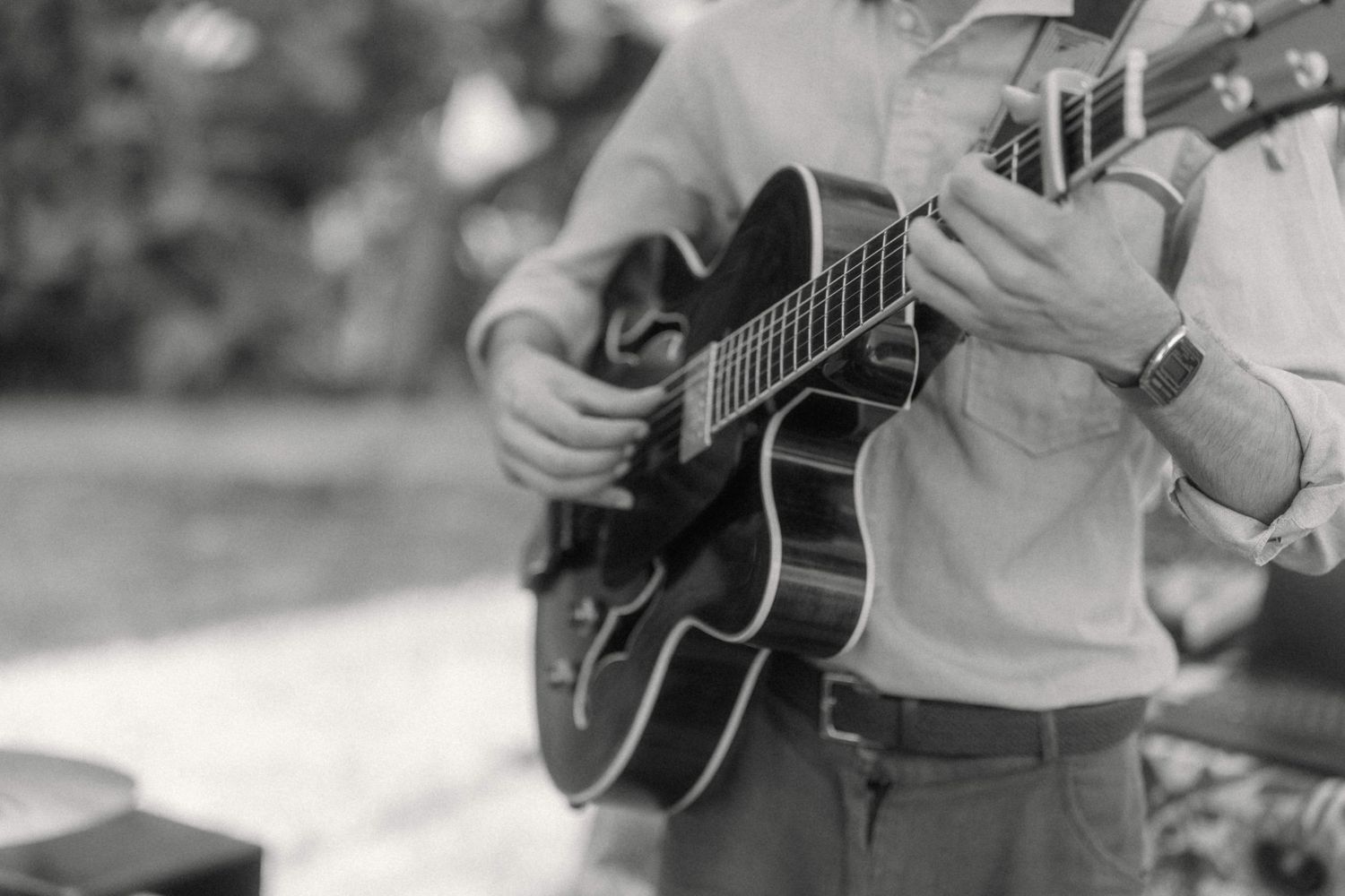 Black and white close-up of a musician playing an archtop jazz guitar at an outdoor wedding reception.