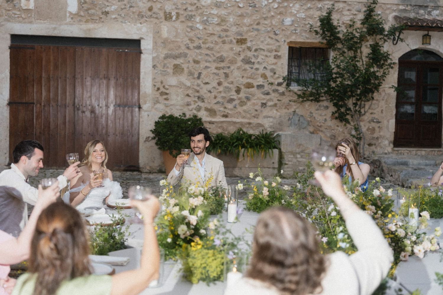 Wedding guests raising glasses in a toast to the groom at a rustic stone venue reception dinner.