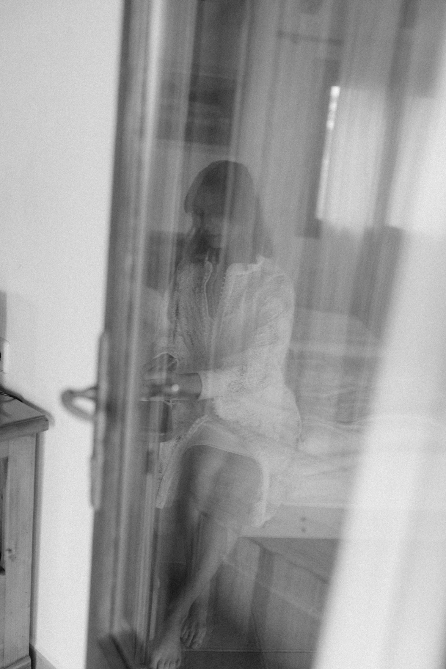 Blurred black and white reflection of a woman in white robe sitting by a window.