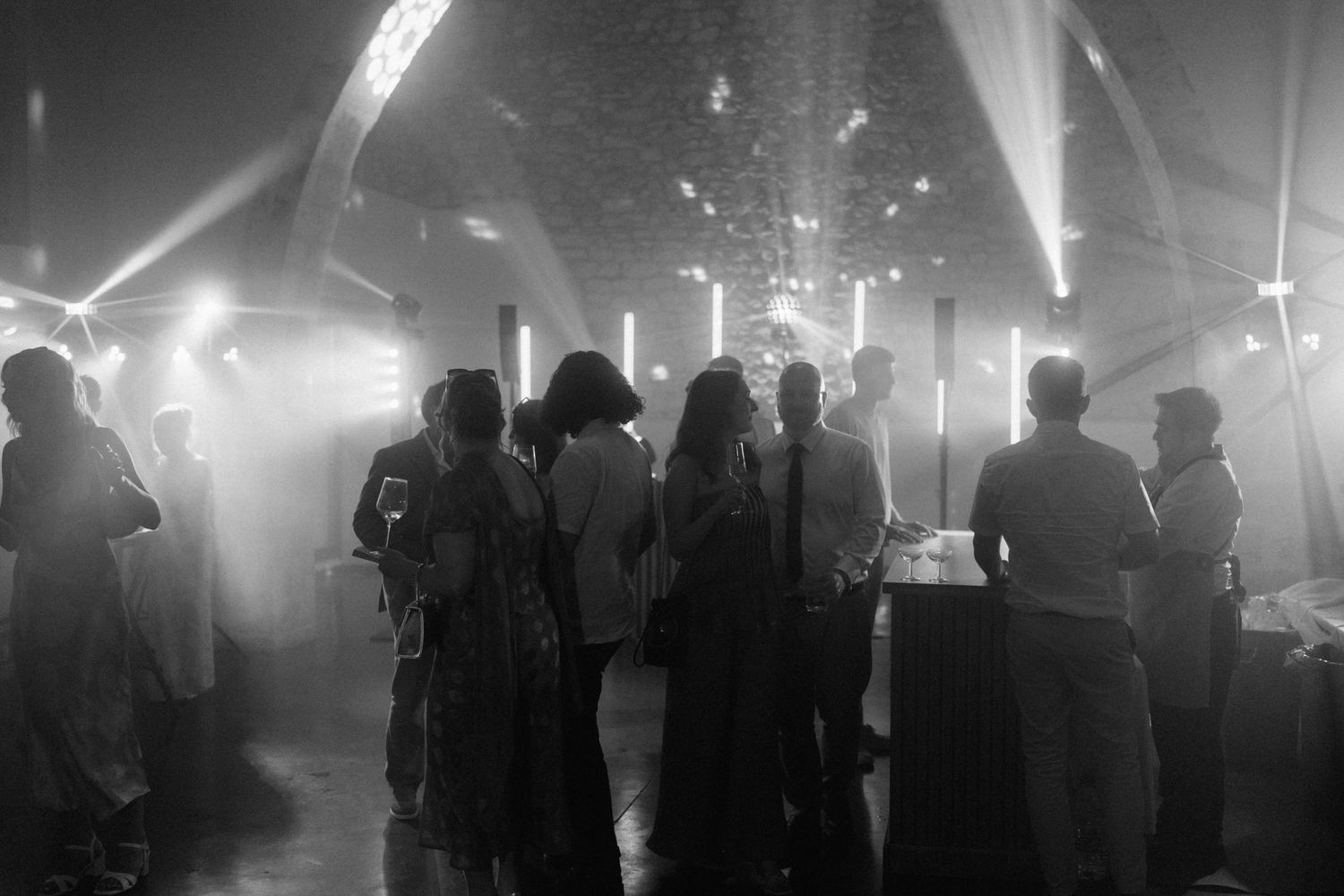 Black and white photo of guests mingling at an elegant evening event with atmospheric lighting and fog effects.