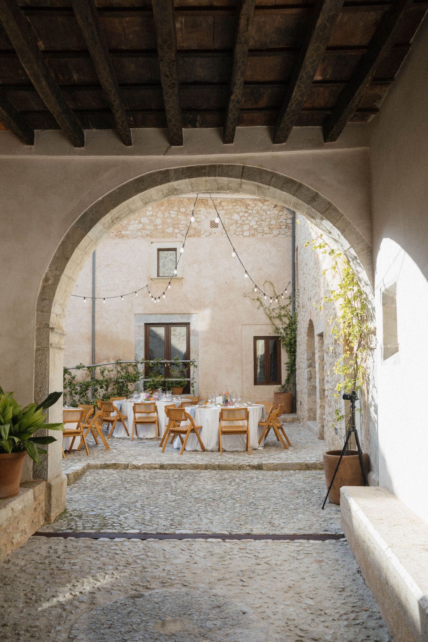 Elegant outdoor wedding reception set in a rustic stone courtyard viewed through an arched doorway with string lights.