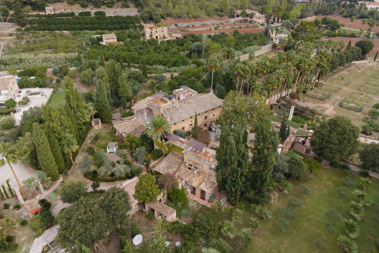 Aerial view of a historic stone villa surrounded by lush gardens, tall cypress trees, terraced grounds and winding paths.
