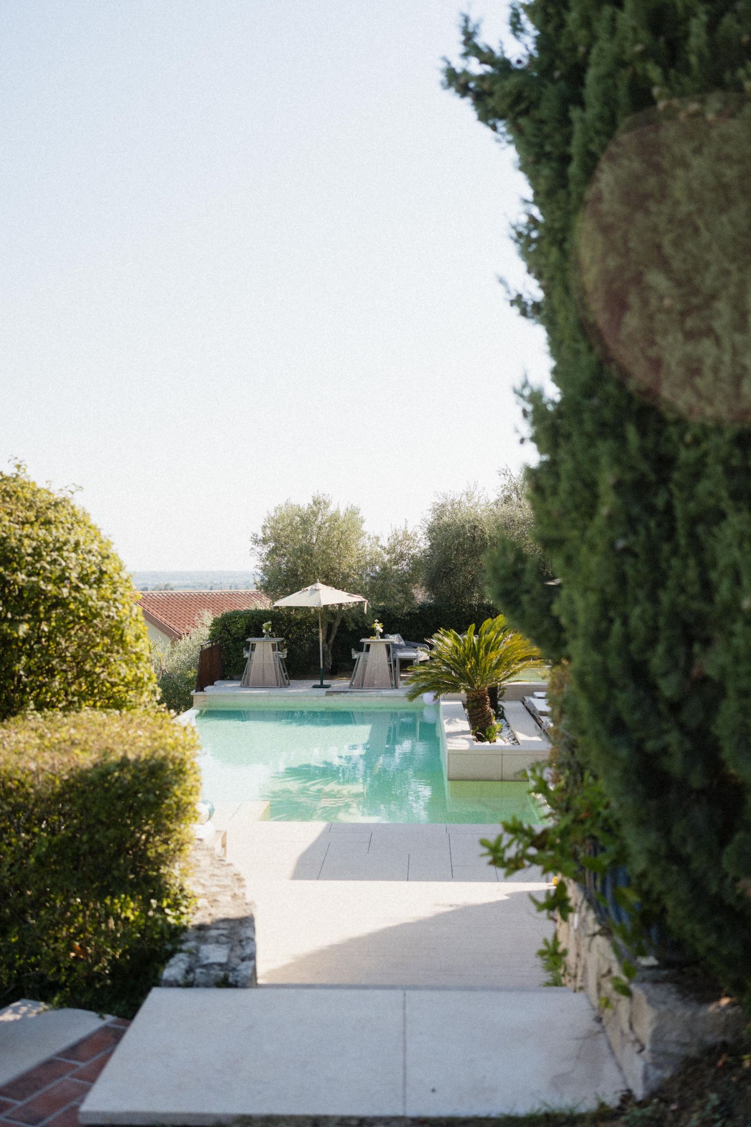 Elegant outdoor pool surrounded by lush greenery and a white umbrella at a Mediterranean villa resort.