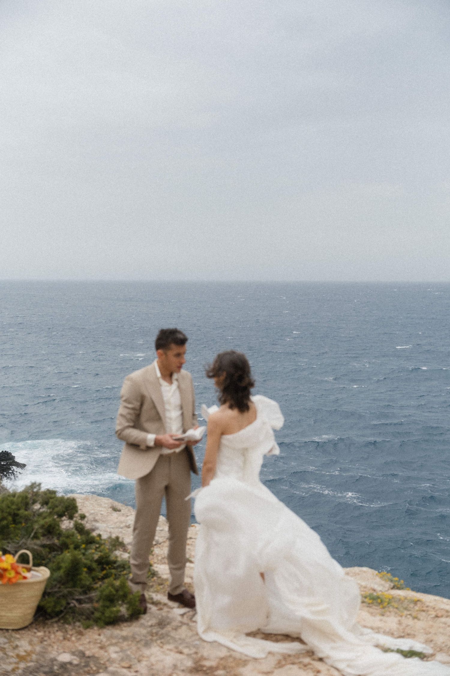 Bride and groom exchange vows on a cliff overlooking the ocean during an intimate outdoor wedding ceremony.