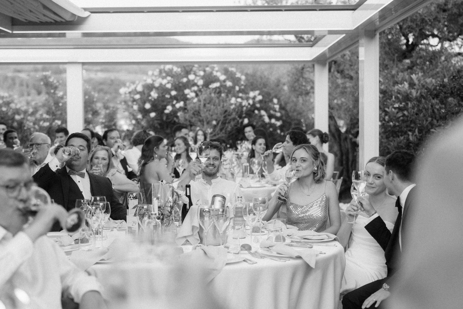 Black and white photo of wedding guests laughing and celebrating at elegantly set tables during a reception.