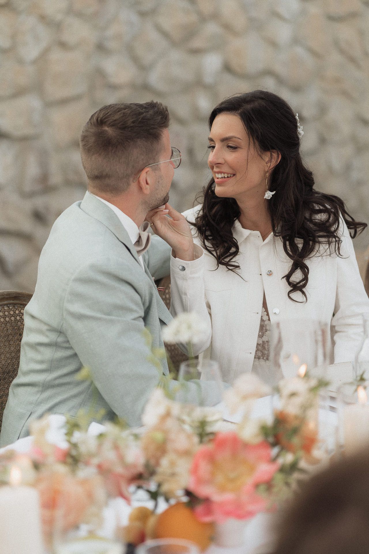 Bride and groom share a tender moment at wedding reception table adorned with peach floral arrangements.