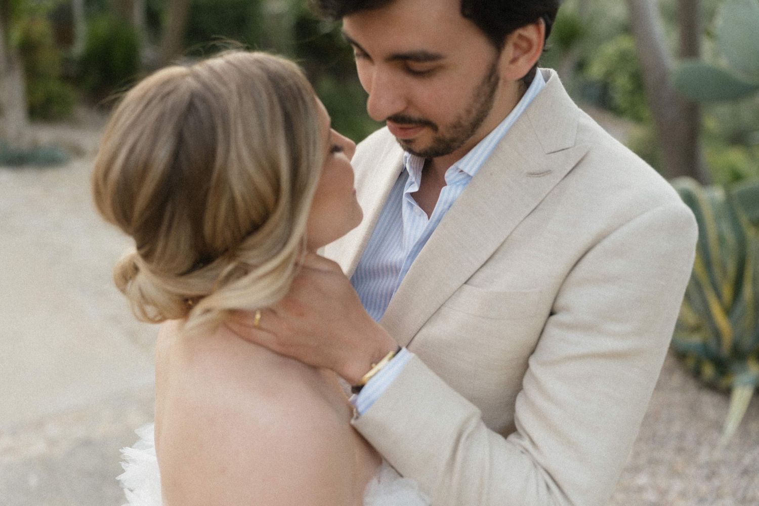 Groom in beige linen suit tenderly embraces bride in an intimate outdoor portrait after their wedding ceremony.