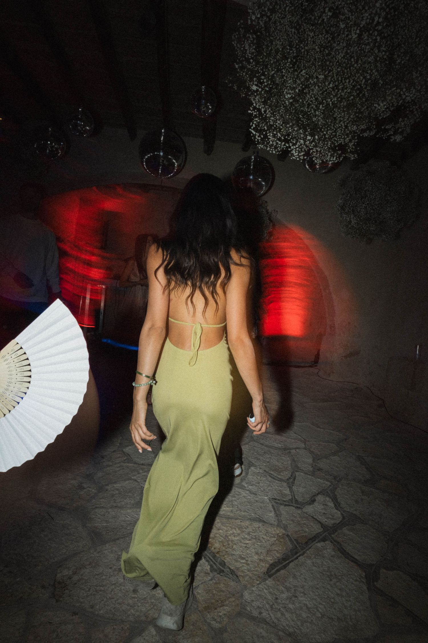 Woman in backless green dress walking through dimly lit outdoor wedding venue at night.