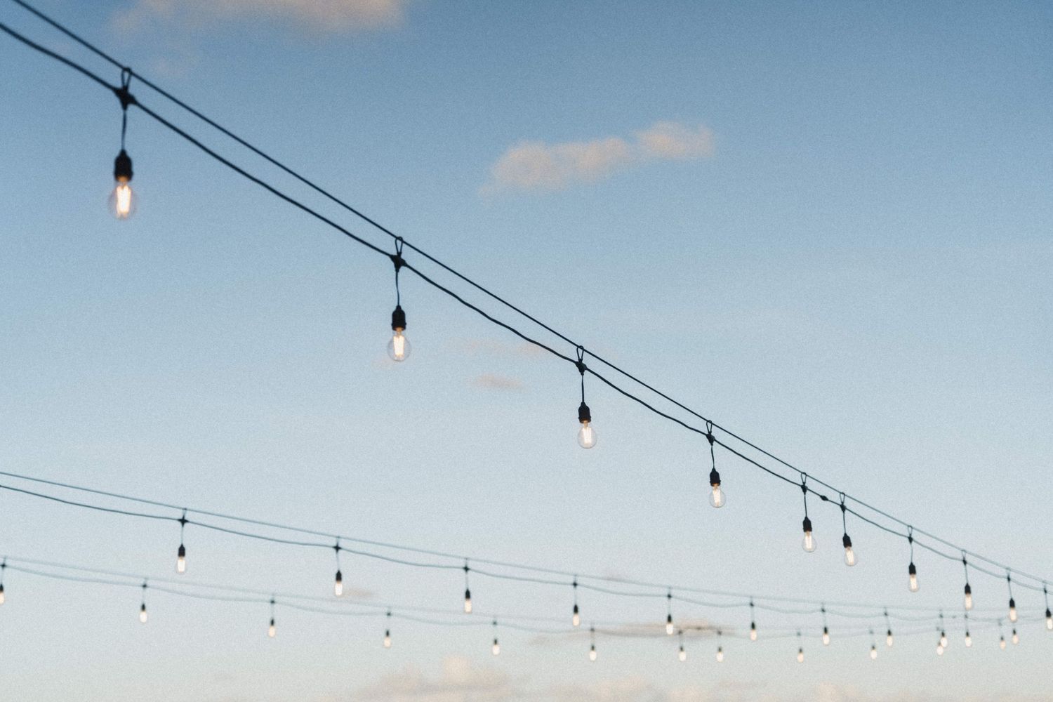 String of Edison bulb lights hanging against a clear blue sky at an outdoor wedding.