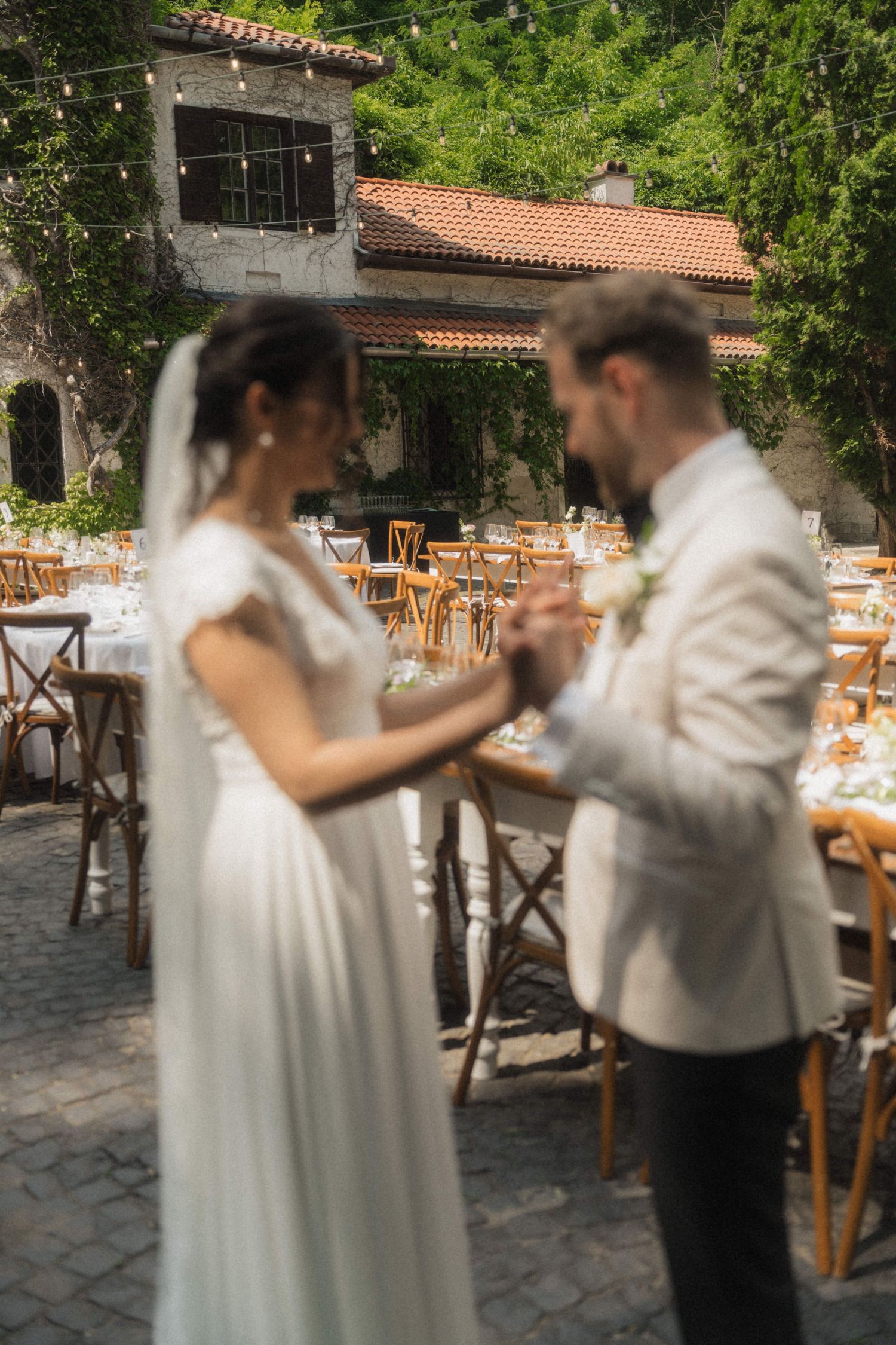 Bride and groom share first dance at outdoor wedding reception with rustic stone venue and string lights.