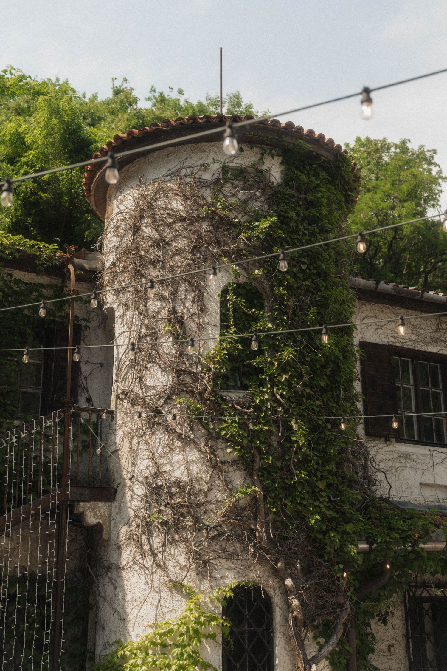 Ivy-covered stone tower with string lights at rustic wedding venue surrounded by lush greenery.