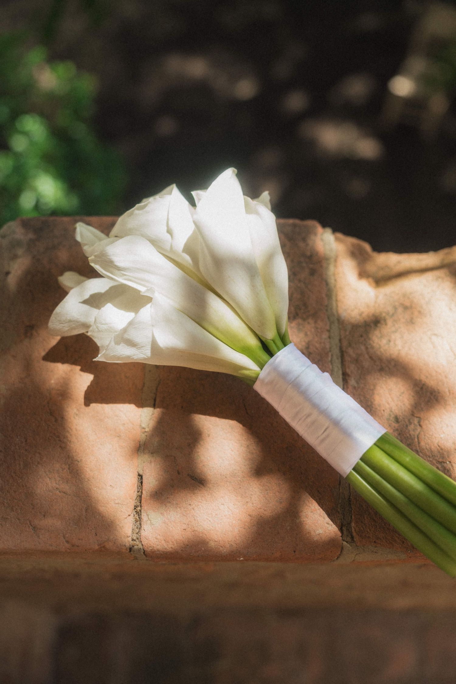 Elegant bridal bouquet of white calla lilies tied with white ribbon resting on rustic stone surface.