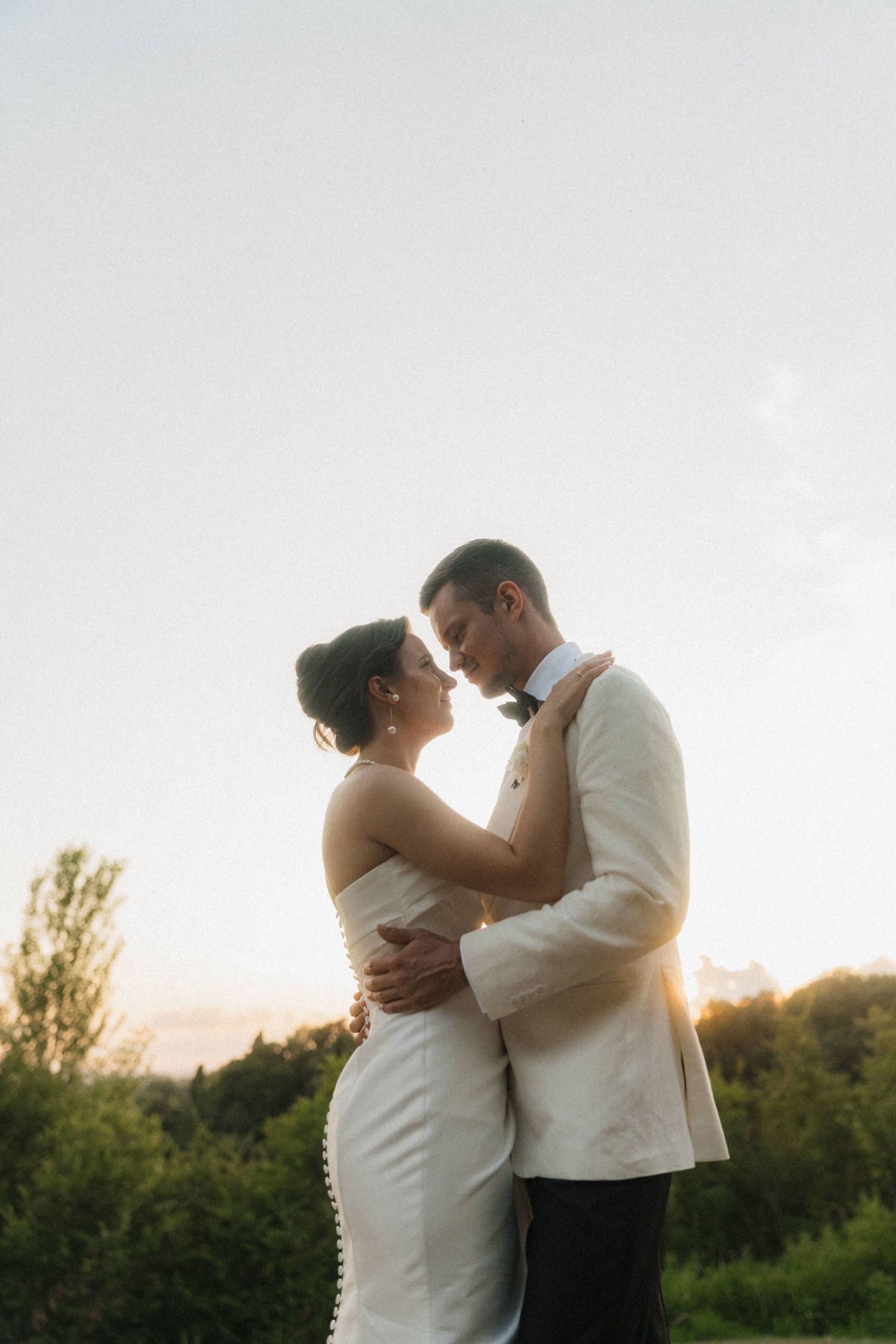 Bride and groom share a romantic embrace at golden hour sunset during their outdoor wedding portrait session.