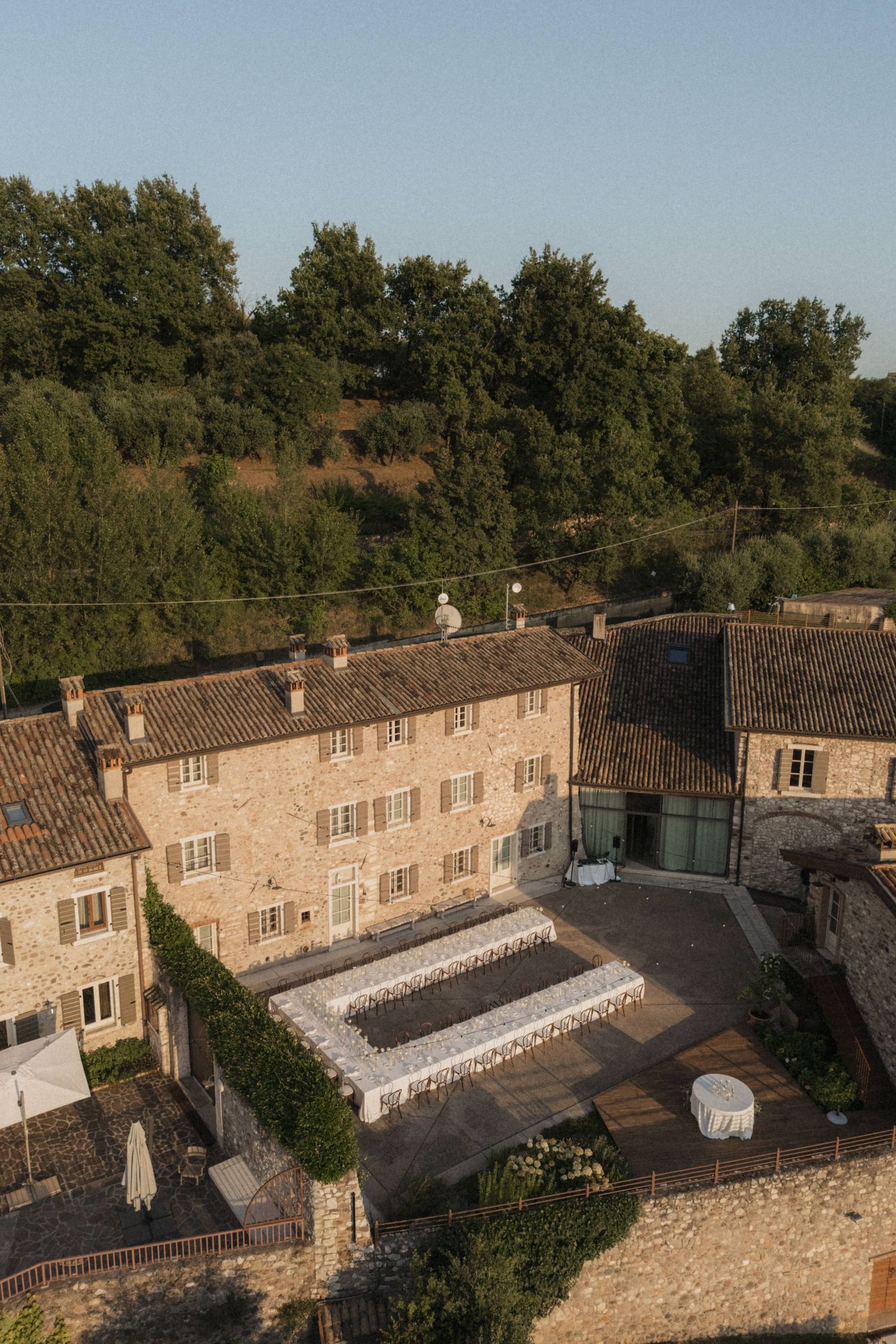 Aerial view of rustic stone Italian villa with long rectangular outdoor wedding reception table.