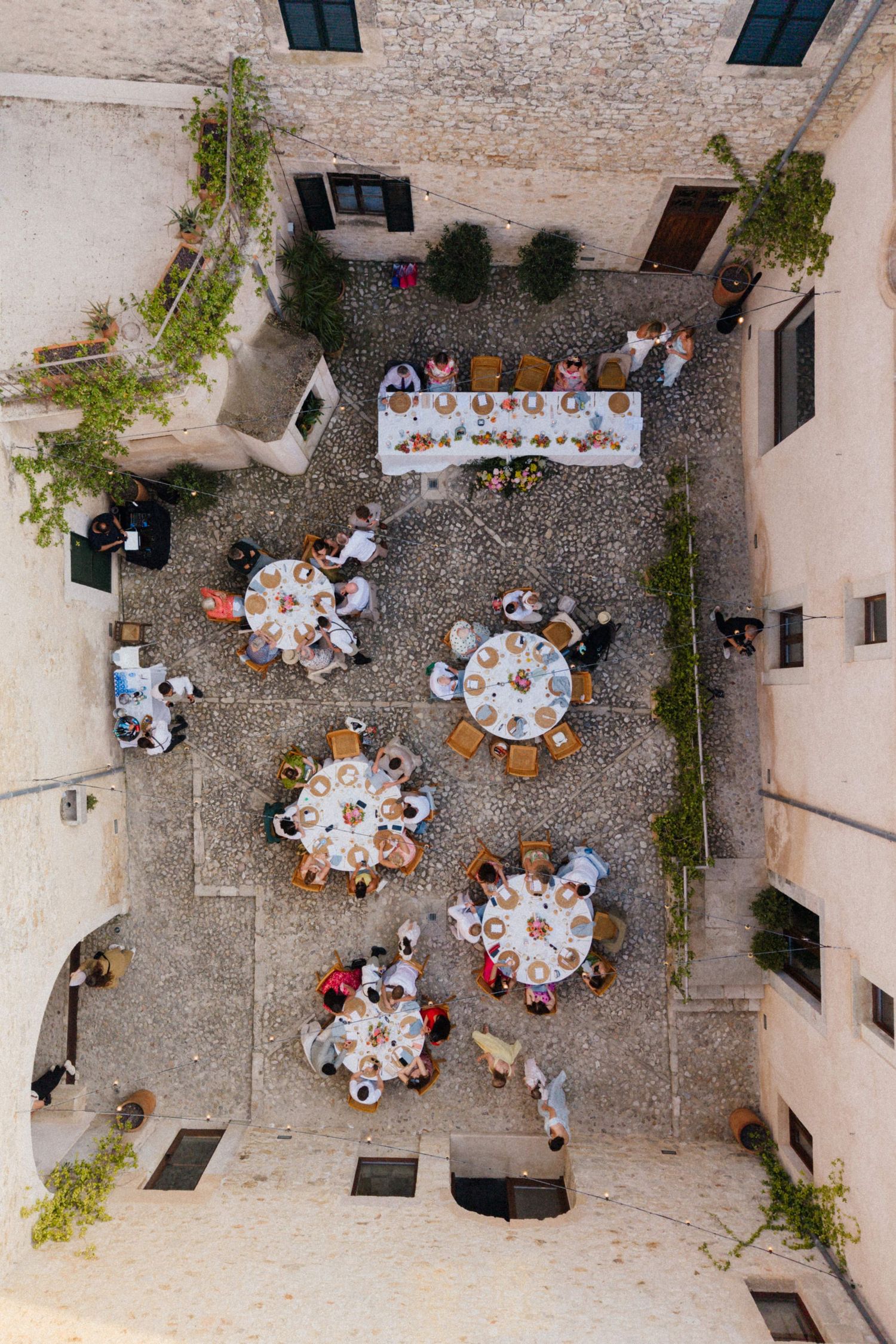 Aerial view of an elegant outdoor wedding reception with round tables in a historic stone courtyard.