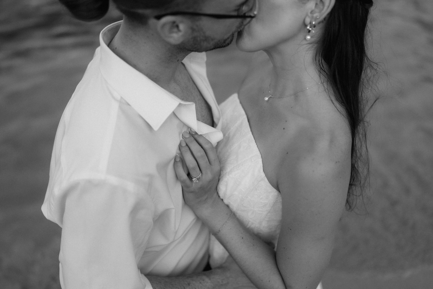 Black and white photo of a couple sharing an intimate kiss, the woman in a lace dress with earrings and the man in a white button-up shirt.