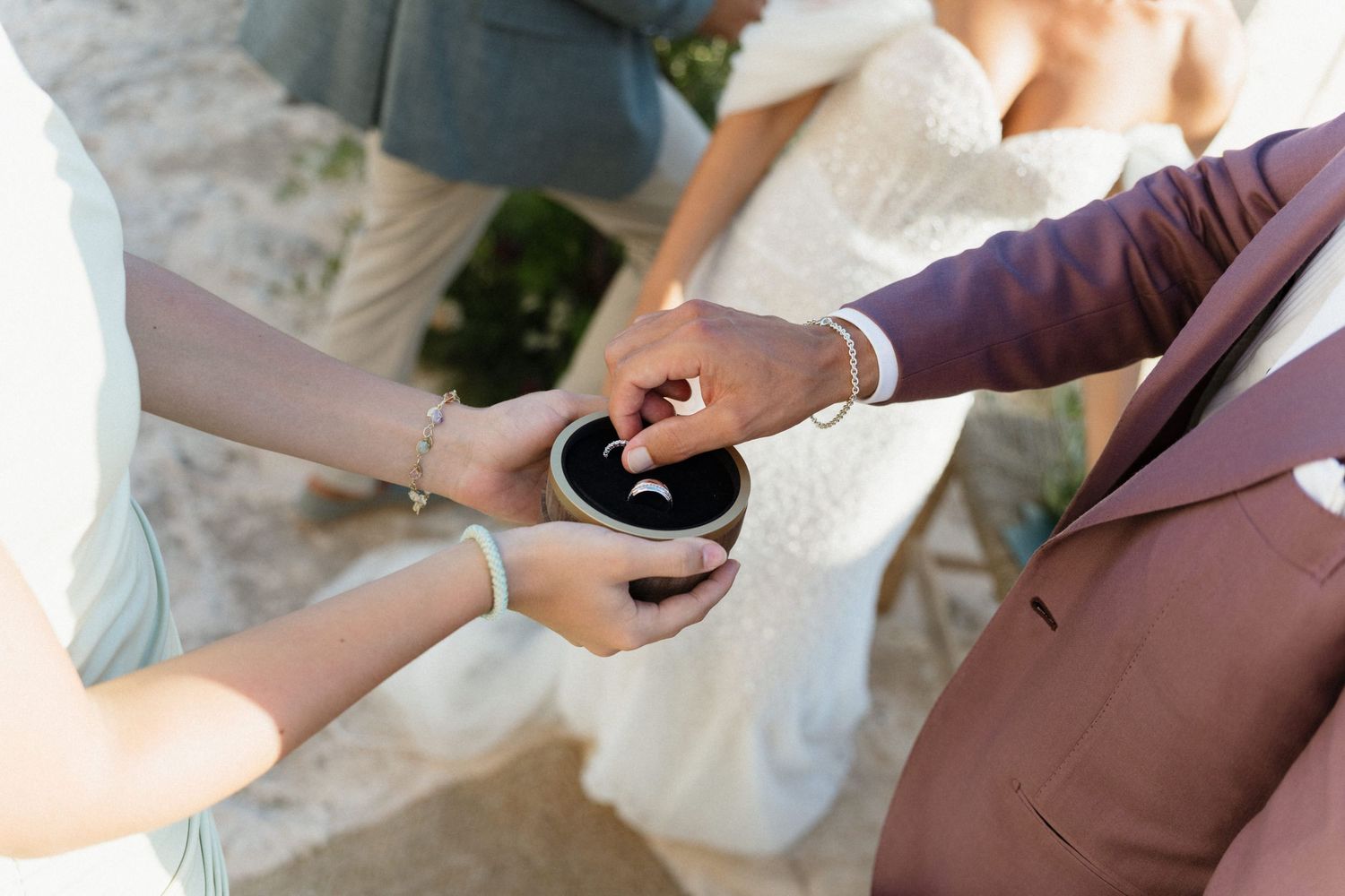 Close-up of a hand placing a ring into a small dark ring box held by another person during a wedding ceremony.