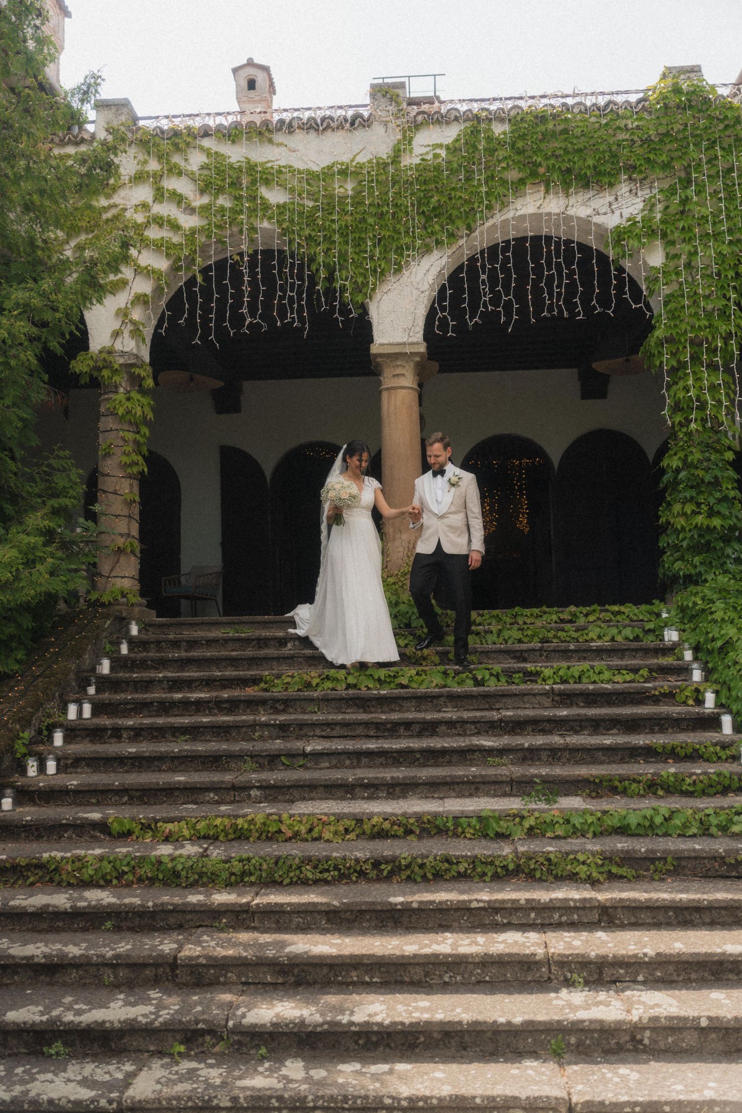Elegant bride and groom descending ivy-covered stone steps at a historic wedding venue.
