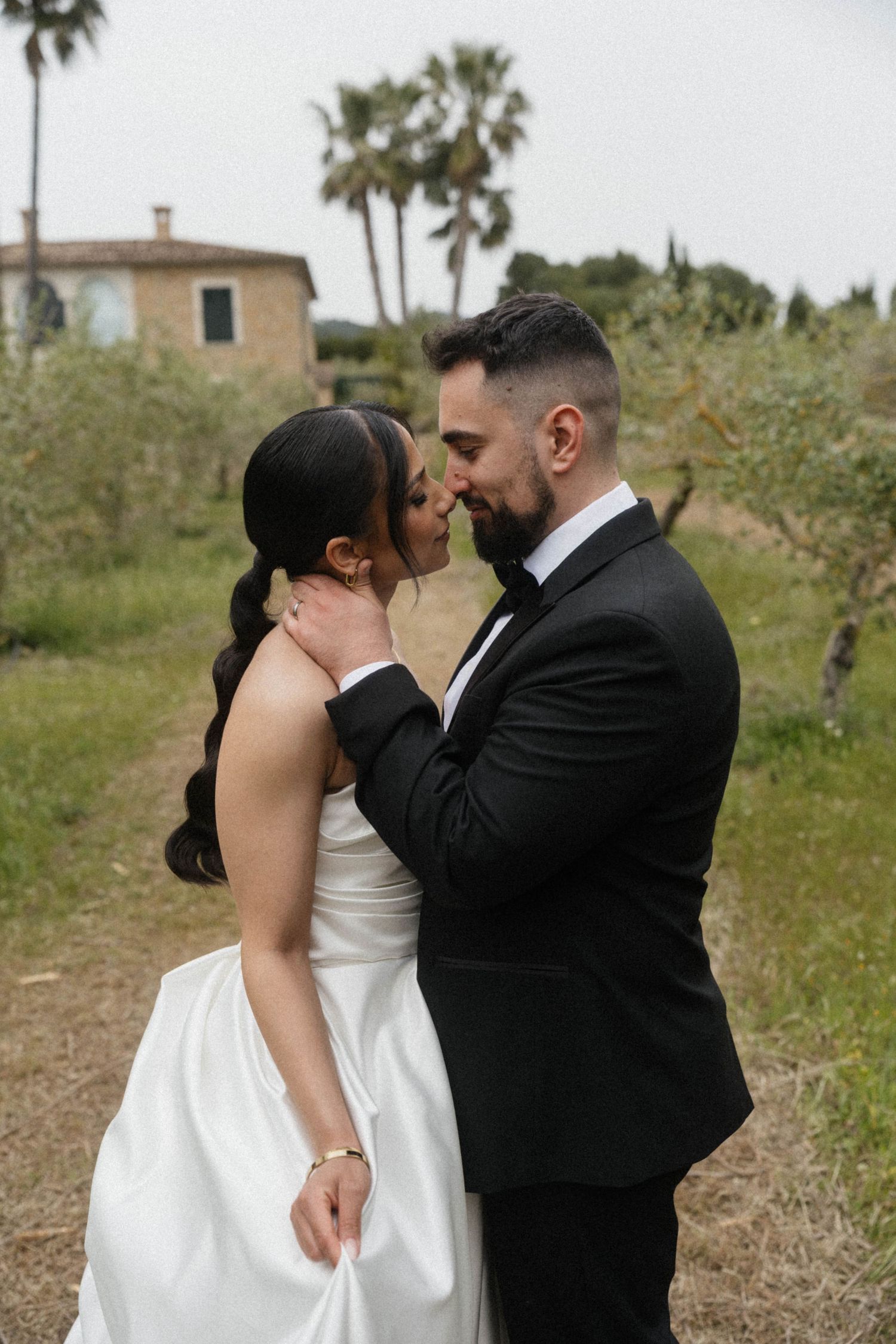 Groom tenderly holding brides face about to kiss in lush green outdoor wedding setting.