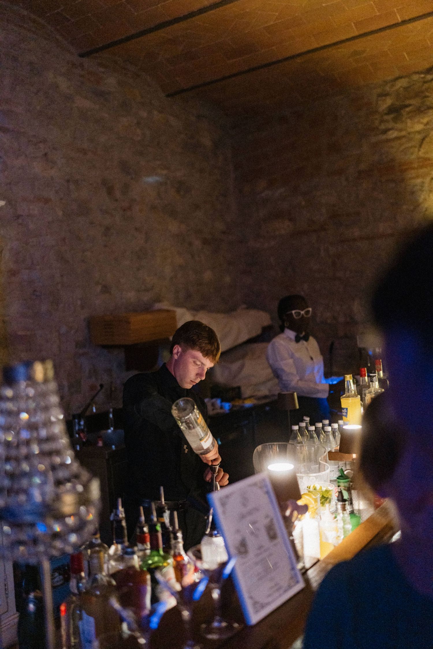 Bartender pouring drinks at a rustic stone-walled bar during a wedding reception celebration.