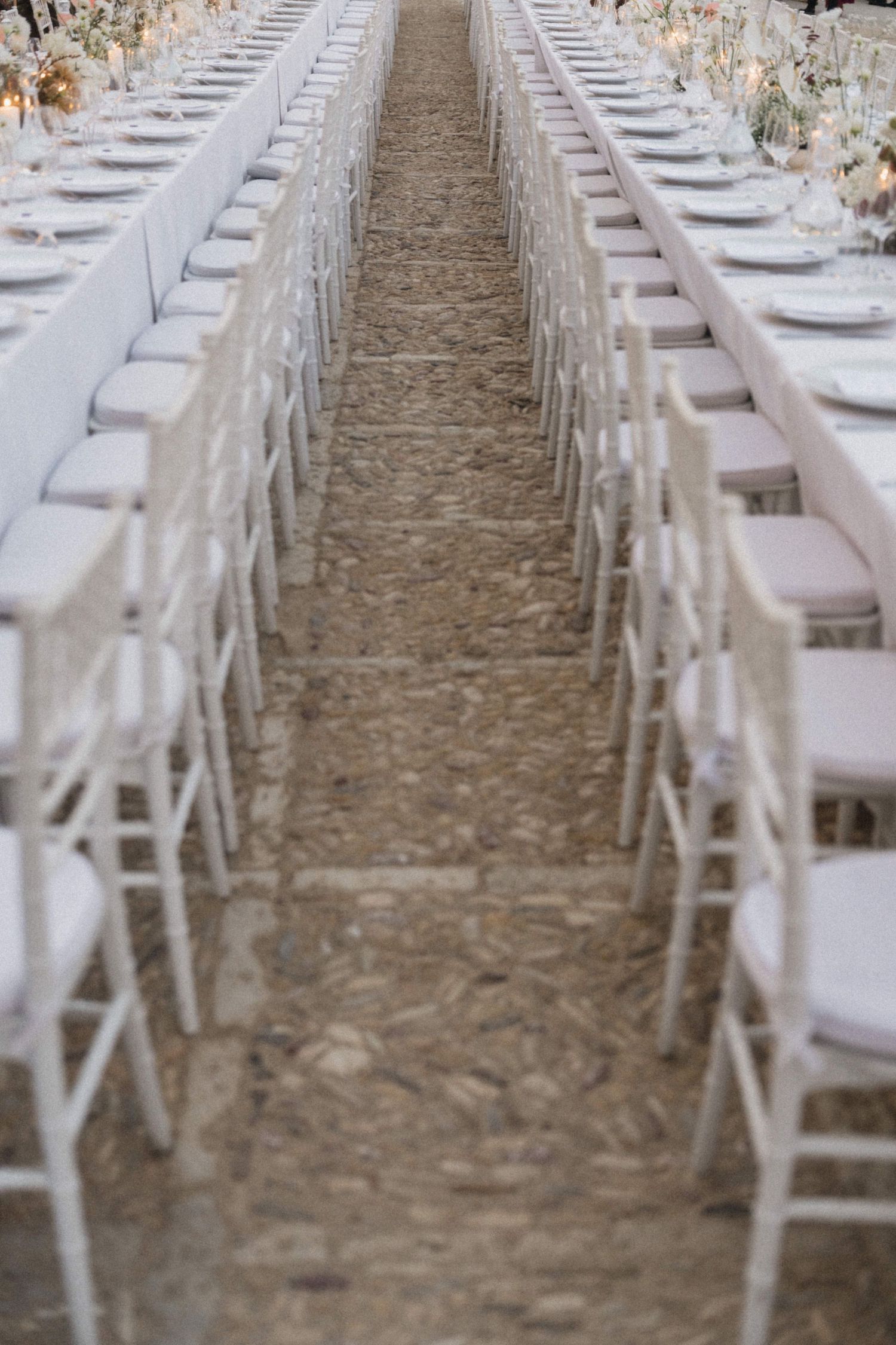 Long rows of white Chiavari chairs and elegant reception tables at an outdoor wedding.