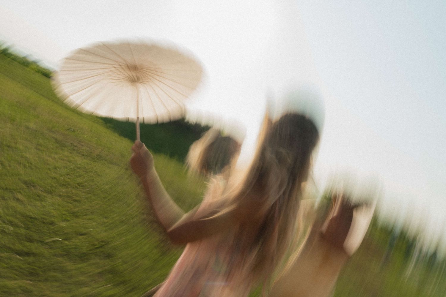 Blurred motion photo of woman holding white parasol umbrella in green meadow at outdoor event.