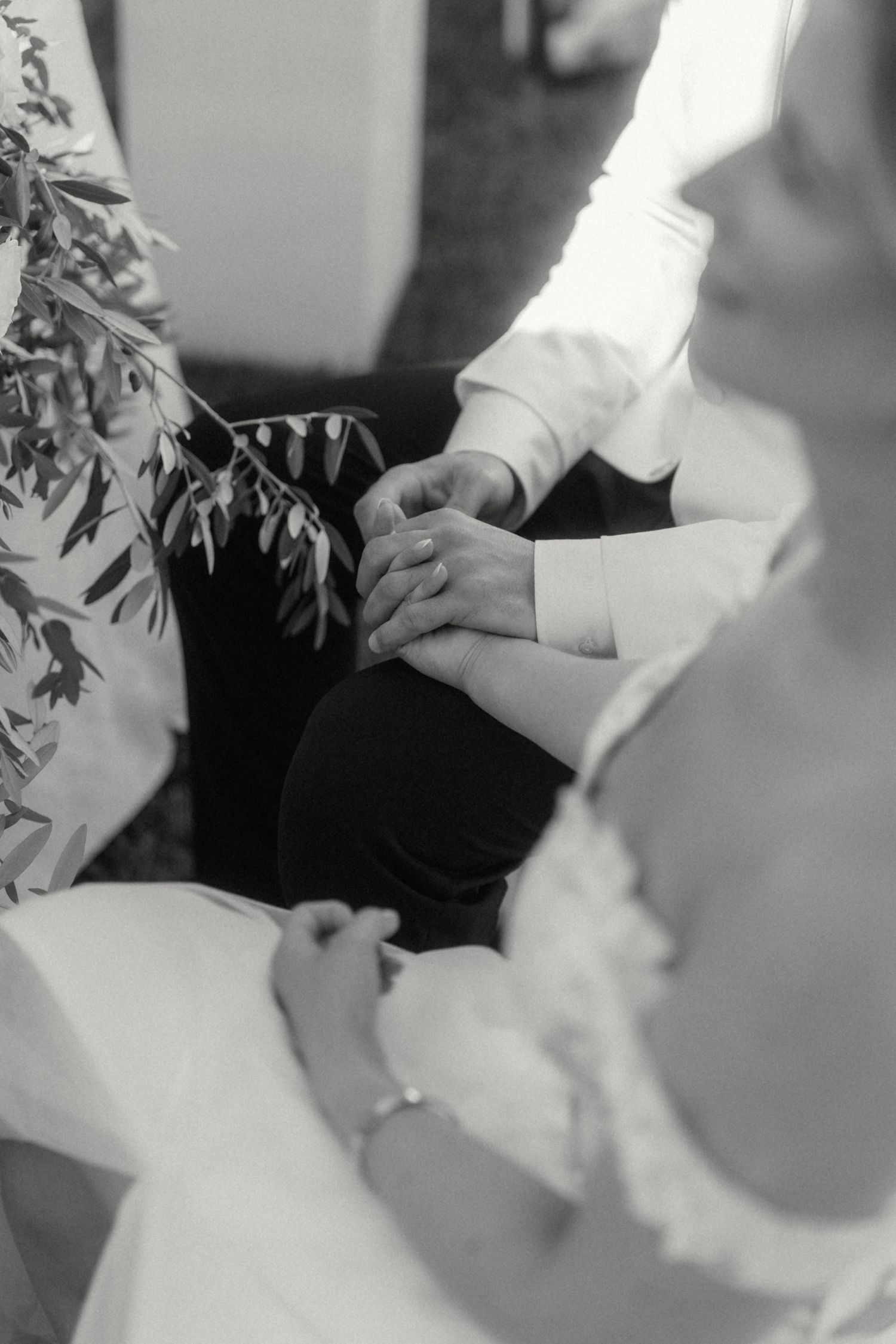 Black and white photo of bride and groom holding hands during wedding ceremony.