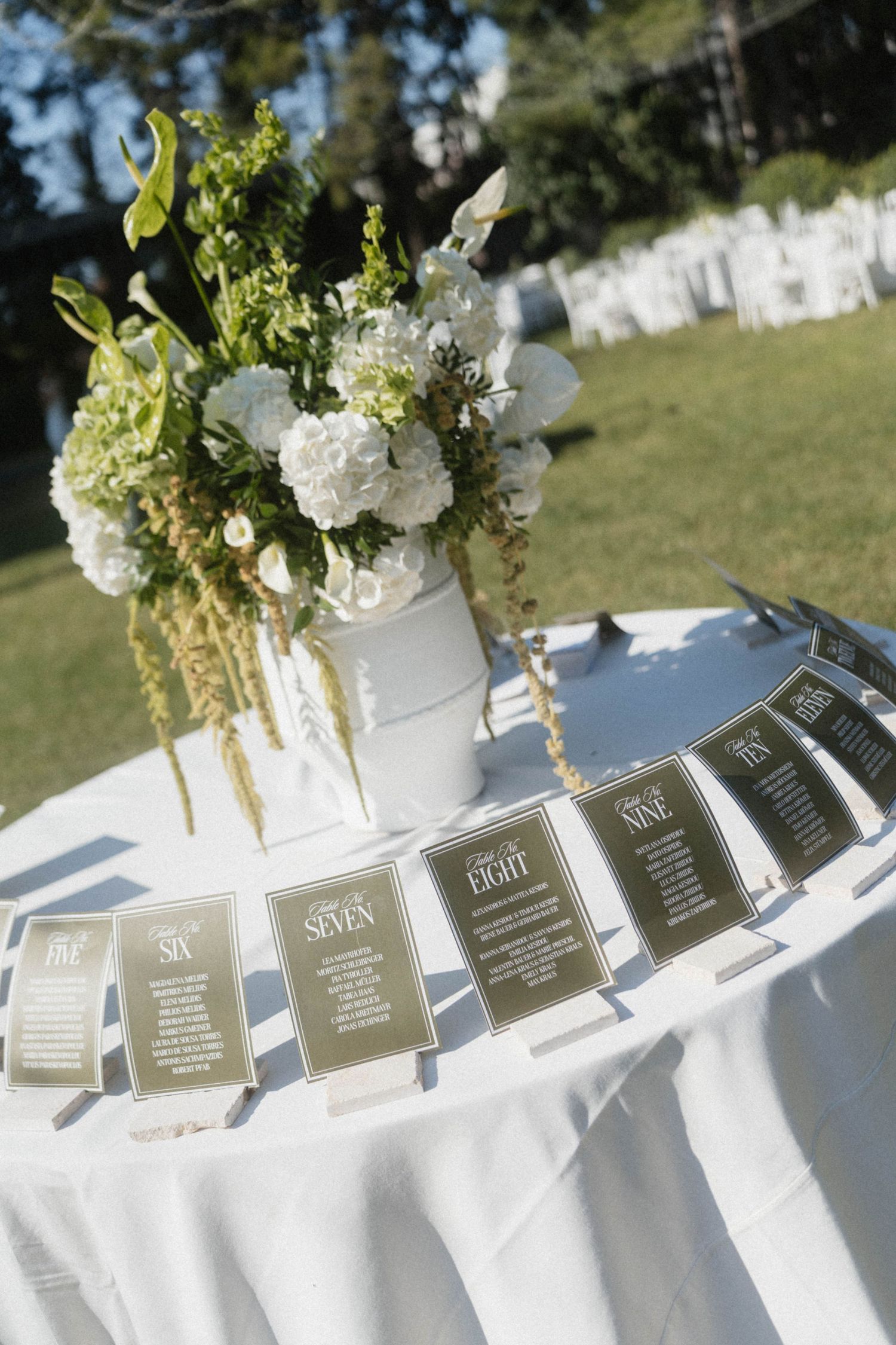 Elegant outdoor wedding seating chart display with numbered table cards arranged on white linen table beside white floral centerpiece.
