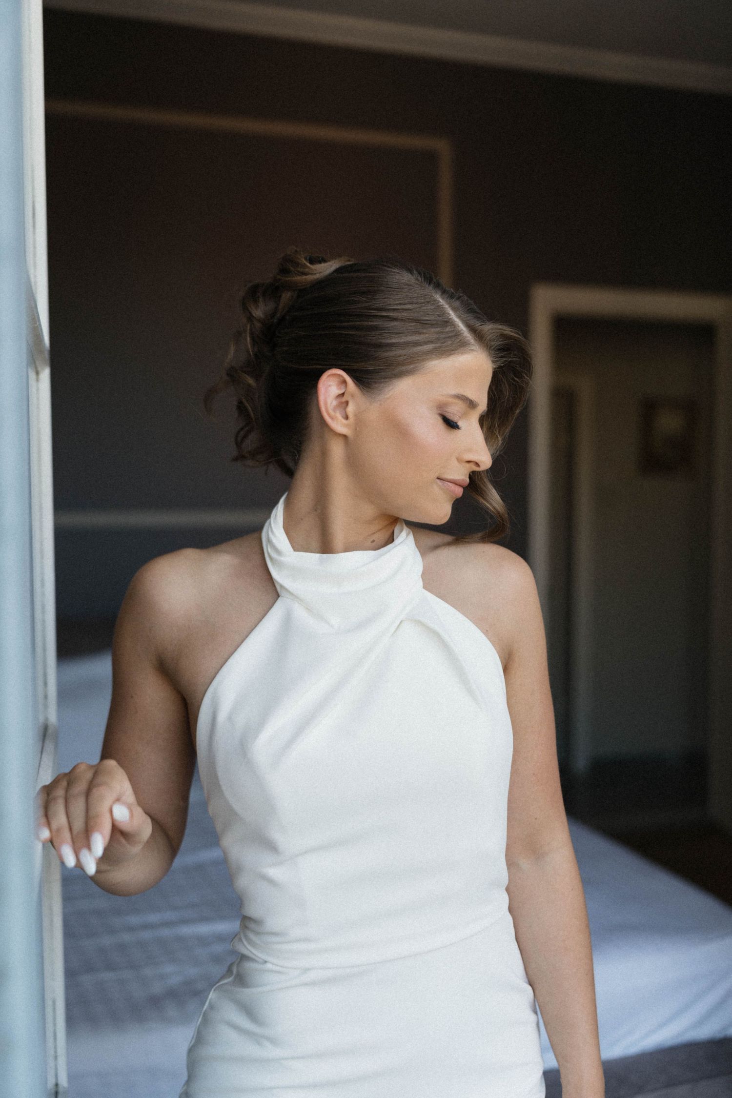 Elegant bride in white halter neck wedding dress posing in a doorway with an updo hairstyle.