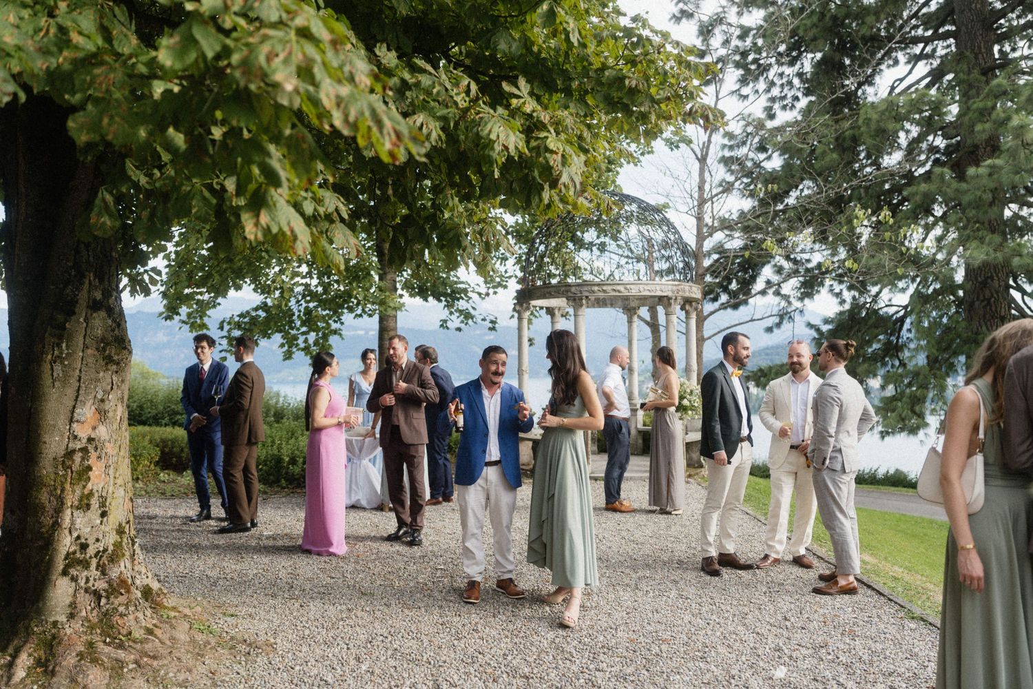 Wedding guests mingling on a gravel path surrounded by trees with a scenic mountain backdrop after the ceremony.