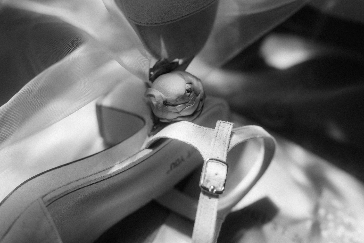 Close-up black and white photo of bridal heels with delicate rose and ribbon wedding accessories detail.
