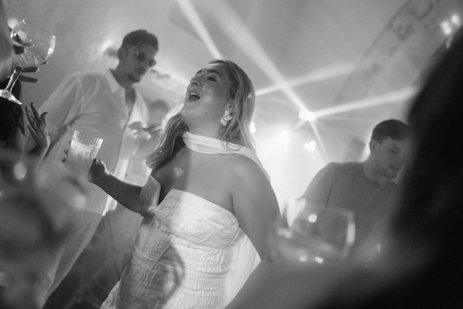Bride in a strapless gown laughing and dancing at a wedding reception in black and white photo.