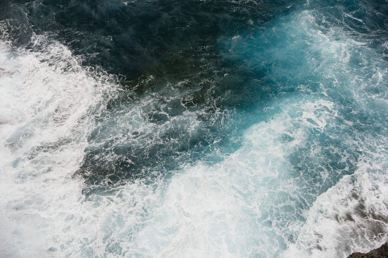 Aerial view of turbulent ocean waves with white sea foam and deep blue-green water.