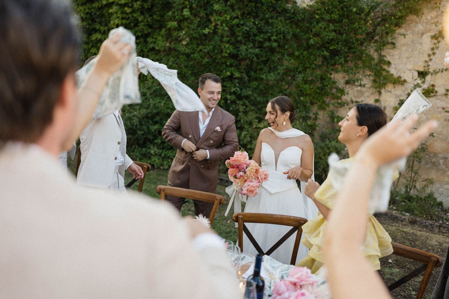 Bride and groom celebrate during outdoor wedding ceremony as guests wave white fabric in the air.