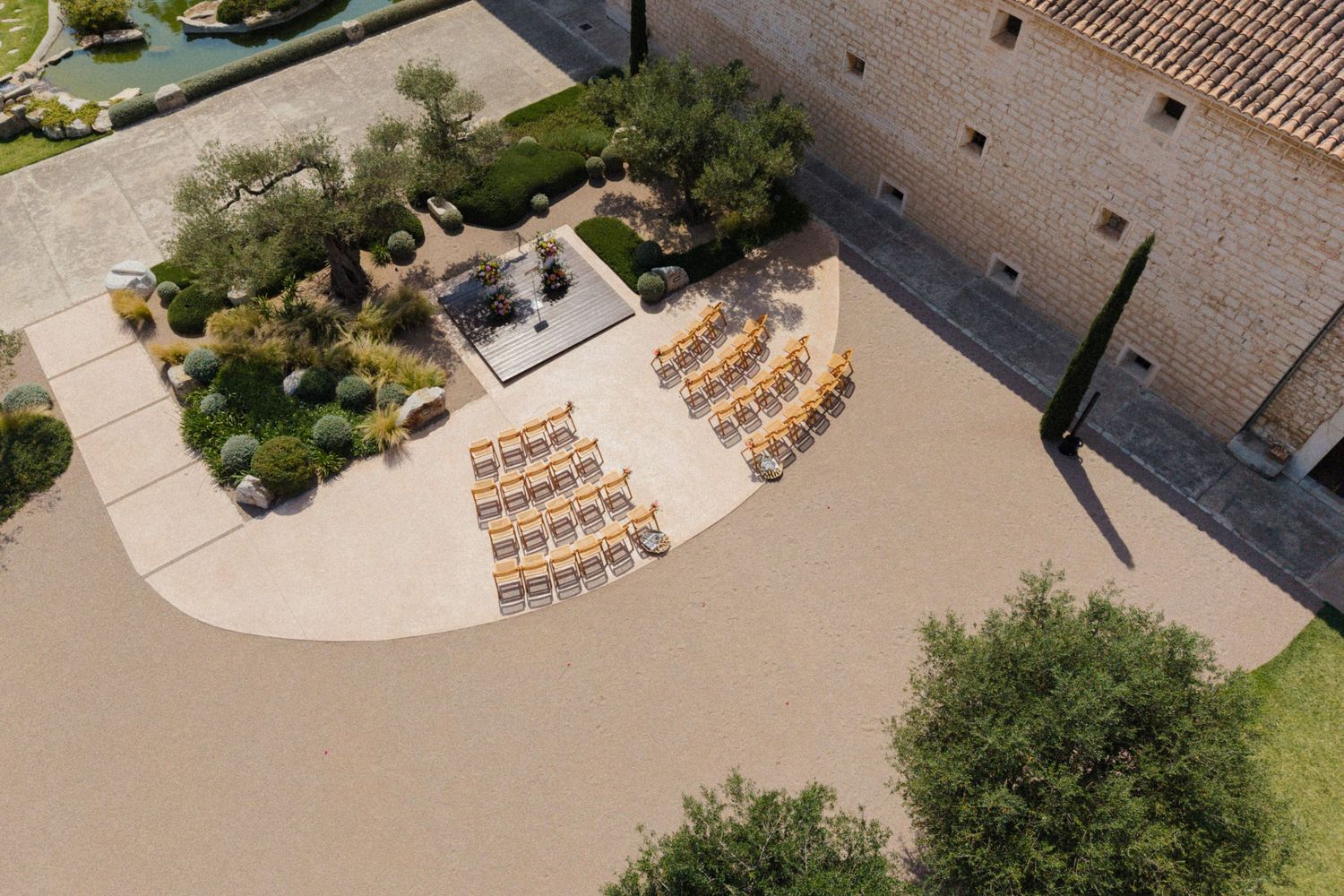 Aerial view of an elegant outdoor wedding ceremony setup with yellow chairs arranged in a semicircle beside a historic stone building.