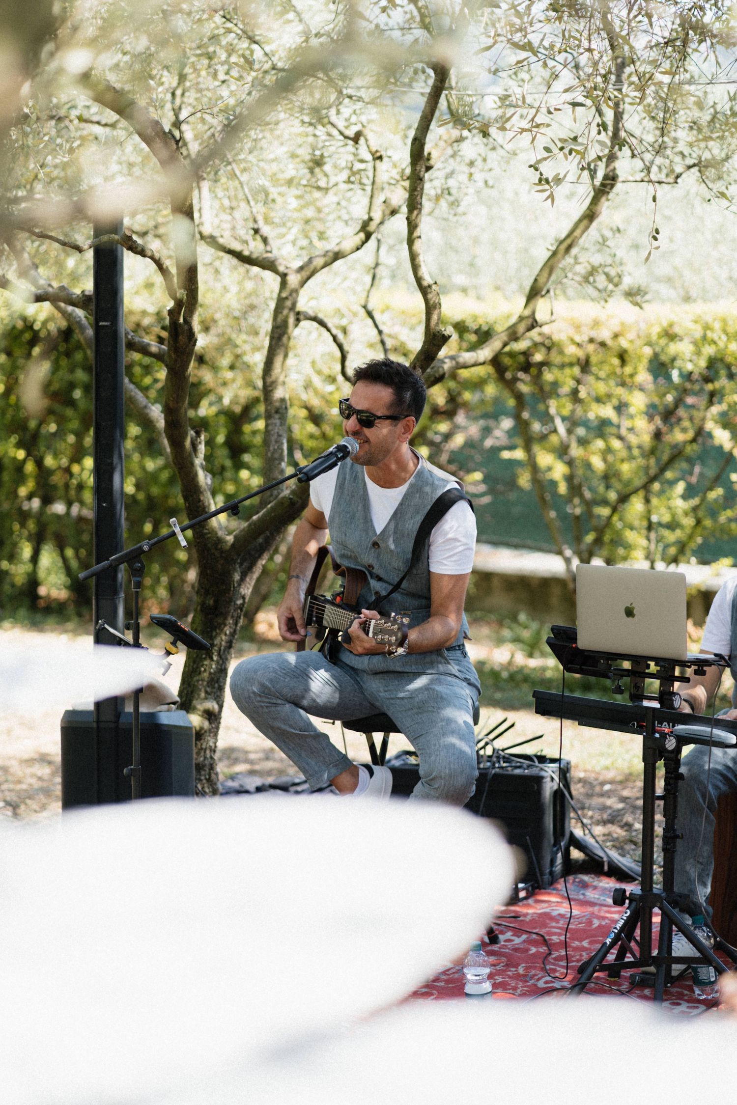 Musician plays acoustic guitar at an outdoor wedding reception surrounded by olive trees.