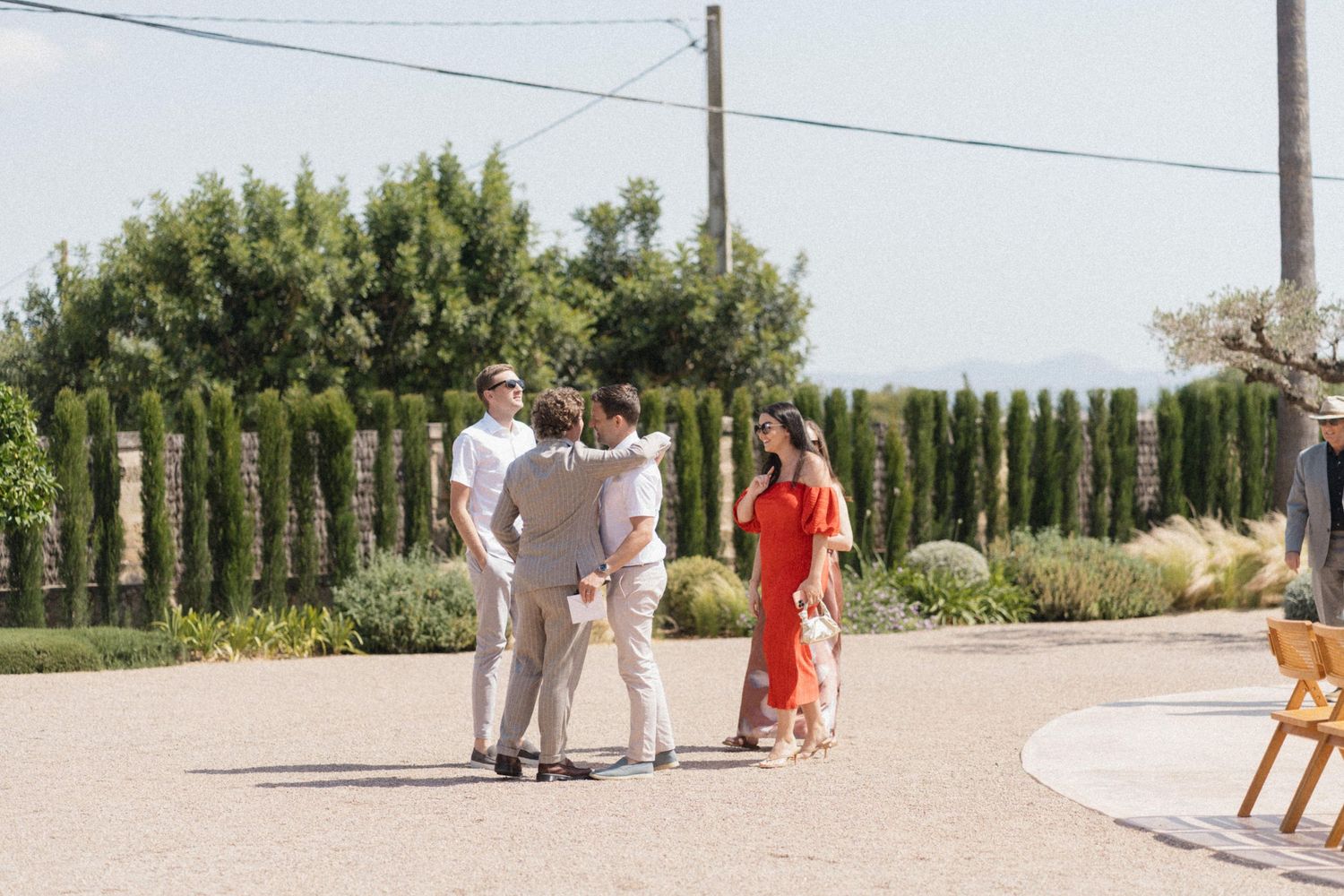 Four guests socializing outdoors at a sunny vineyard wedding venue surrounded by lush greenery.