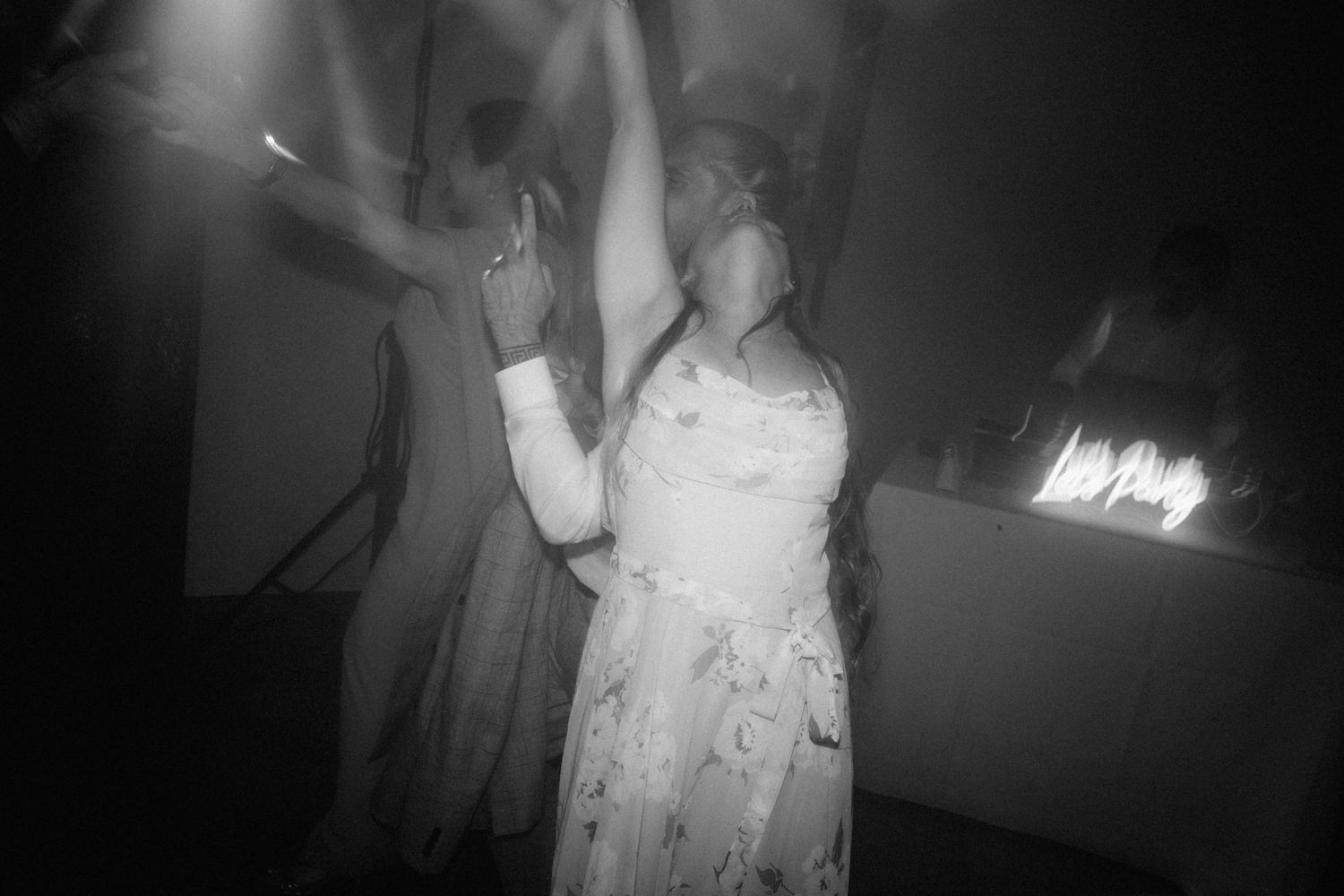Black and white photo of wedding guest dancing joyfully on dimly lit reception dance floor.
