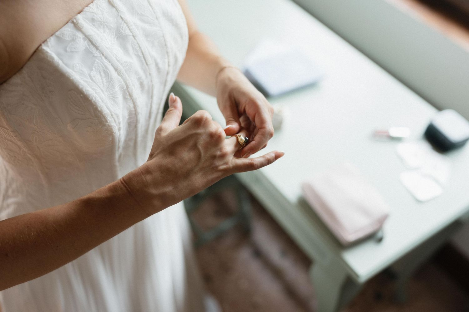 Bride in a white strapless wedding dress adjusts the ring on her finger while standing near a table with small accessories.
