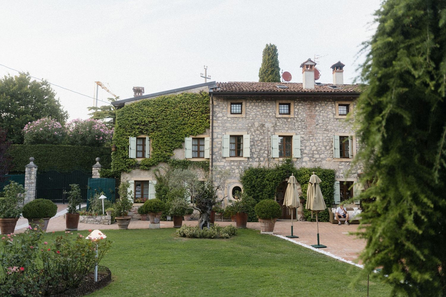 Historic ivy-covered stone villa with manicured gardens and outdoor dining area in the Italian countryside.