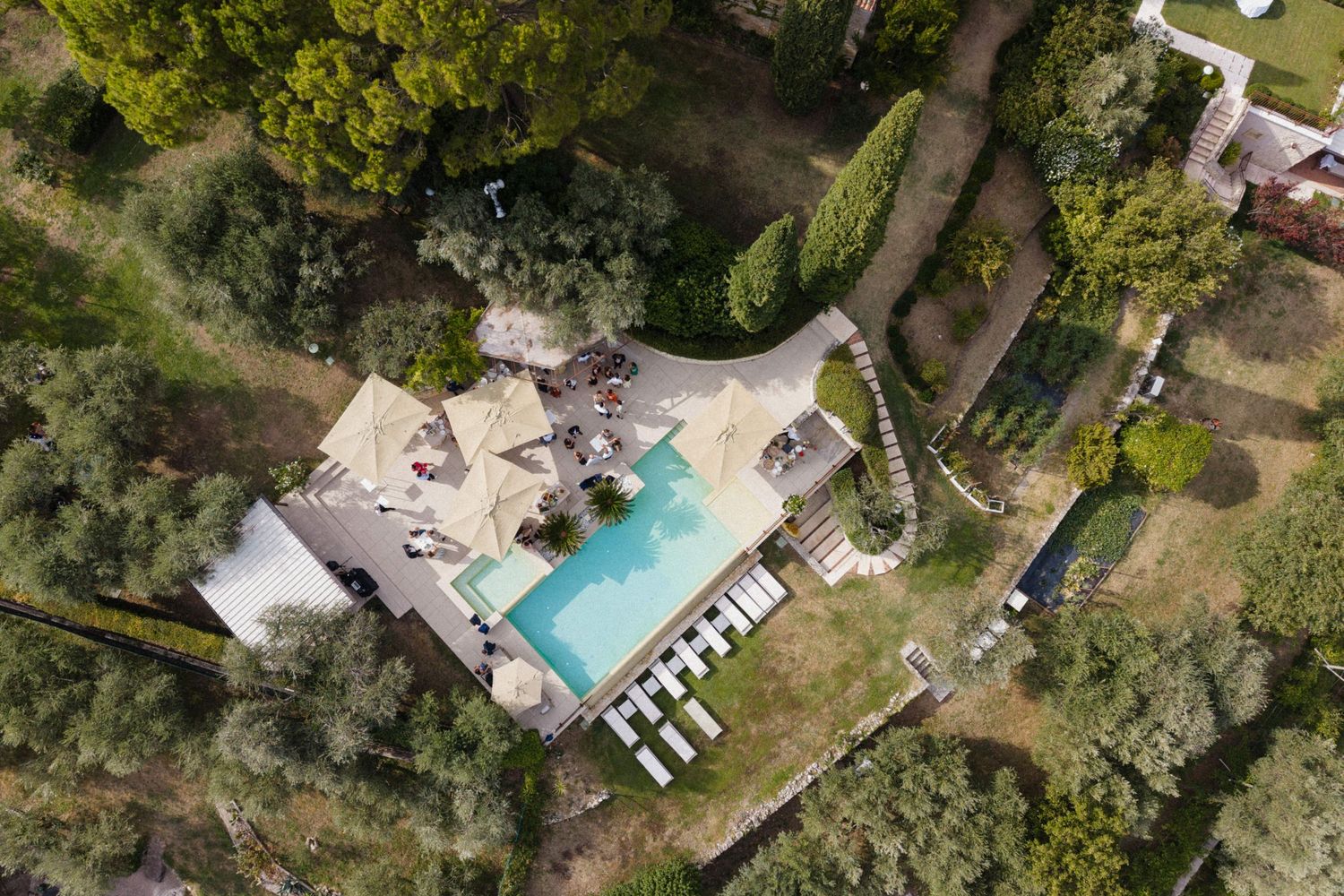 Aerial view of a luxury villa with a turquoise swimming pool surrounded by lush green trees and manicured gardens.