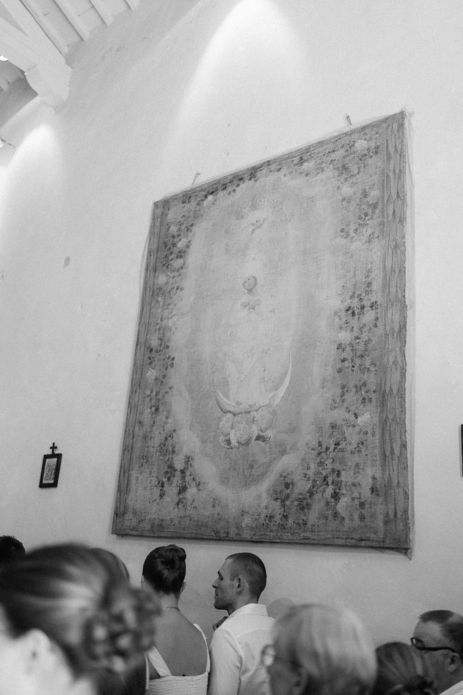 Bride and groom exchange vows beneath a large vintage tapestry in a historic chapel.