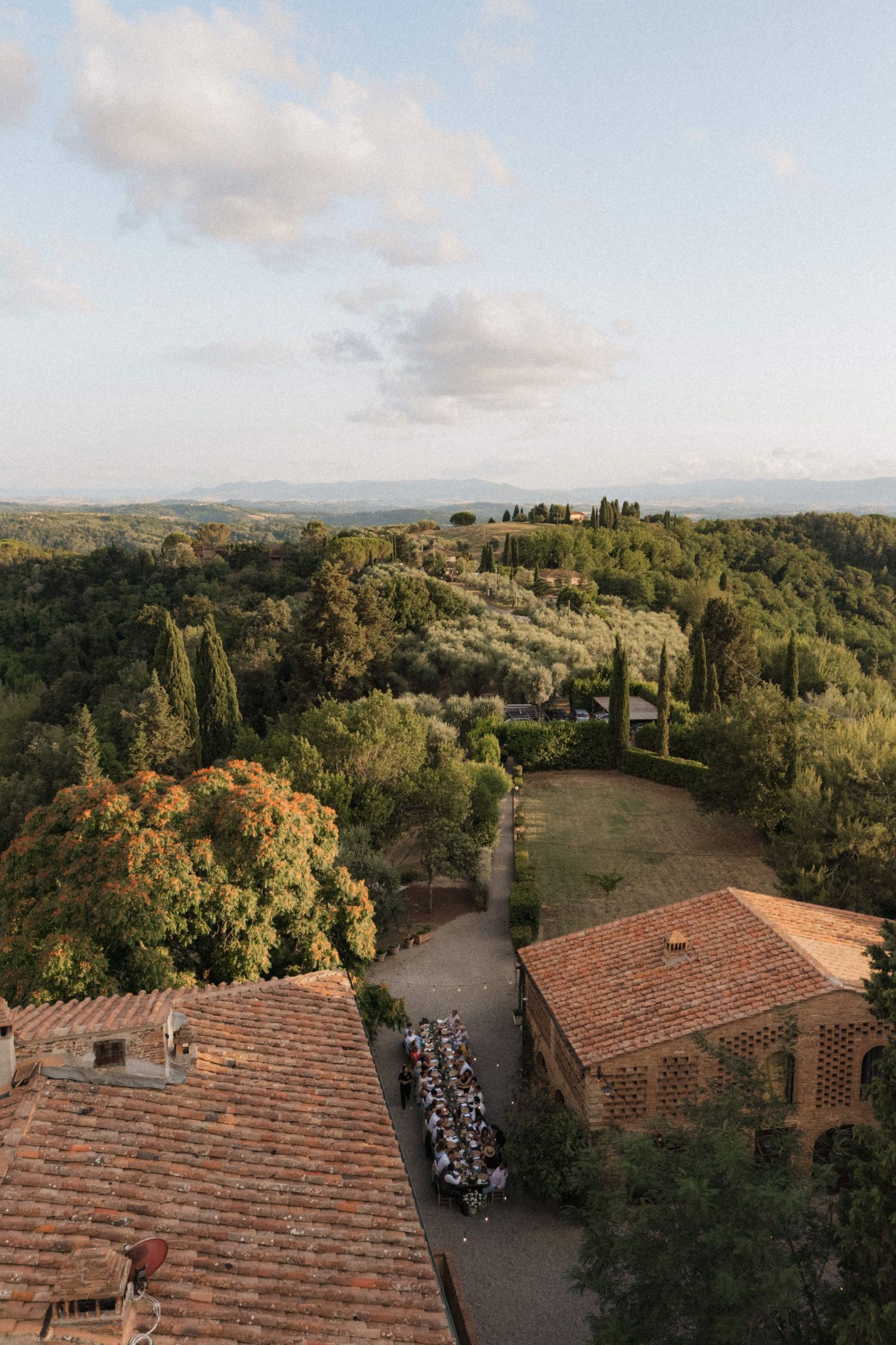 Aerial view of a Tuscan villa wedding reception with long dining tables surrounded by rolling green countryside.