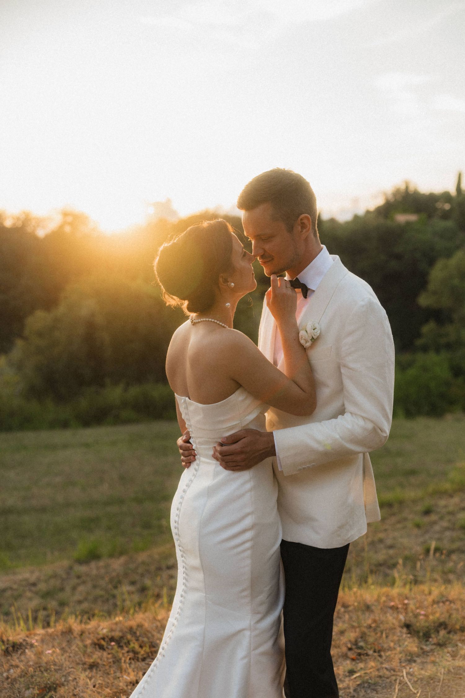 Bride and groom embrace romantically at golden sunset in scenic Tuscan countryside field.