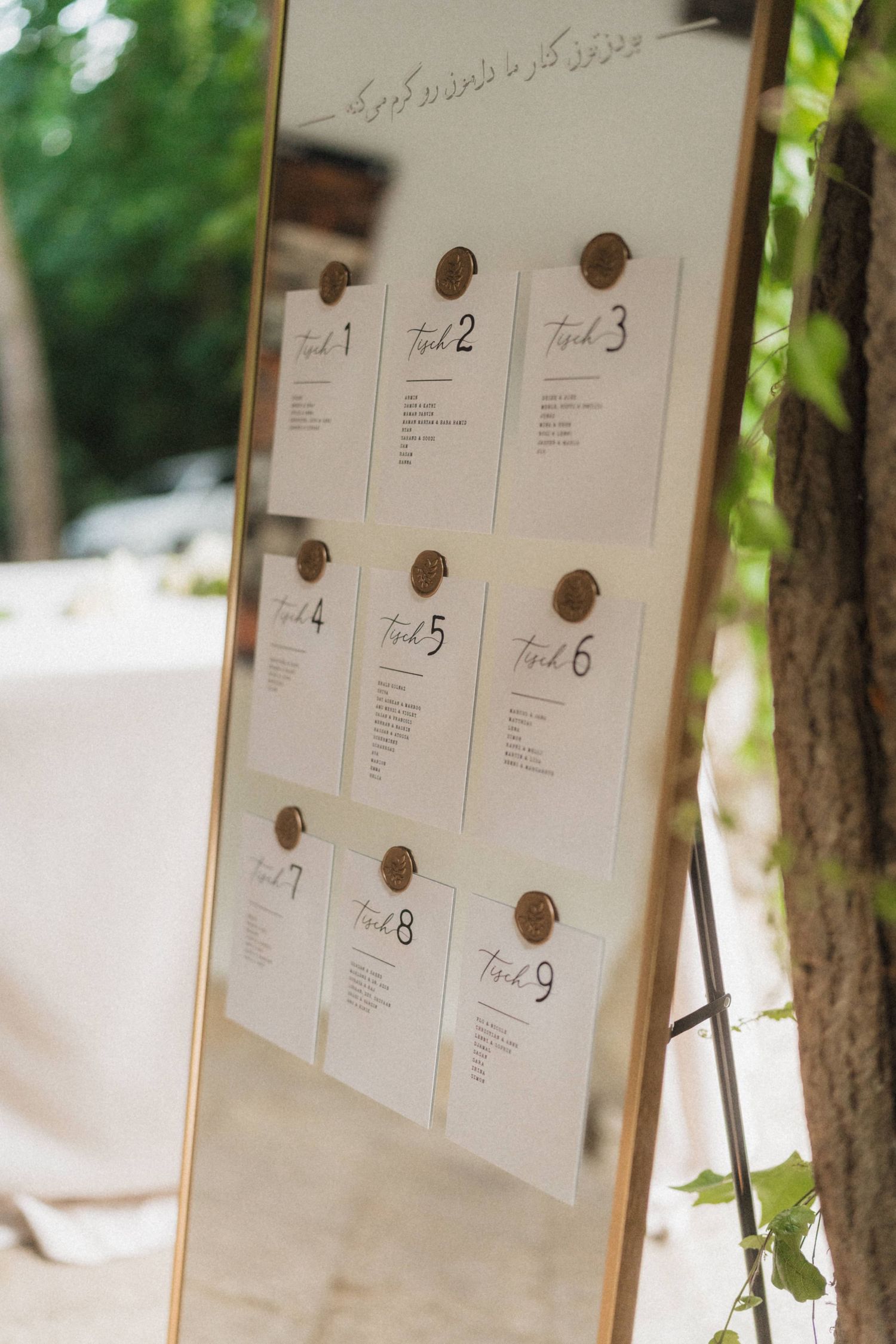 Gold-framed wedding seating chart display with nine numbered table cards pinned outdoors.